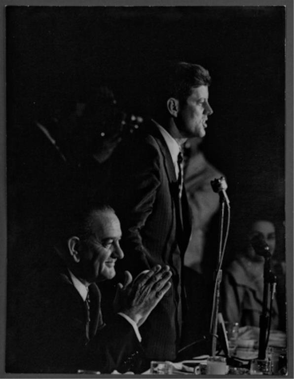 Photograph of John F. Kennedy at the DNC: (1) Large format photograph of John F. Kennedy addressing the crowd at the Democratic National Convention with Lyndon Johnson seated at his side, 13 3/4 x 10 1/2 inches, stamped "photo by Bill Bridges