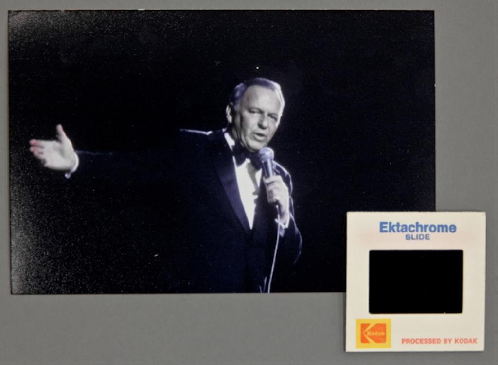 Frank Sinatra: (1) 35mm color transparency of Frank Sinatra, together with (1) 4 x 6 inch photograph reprint. Sinatra is on stage holding a microphone, one arm extended. From the "Main Event" tour 1974.