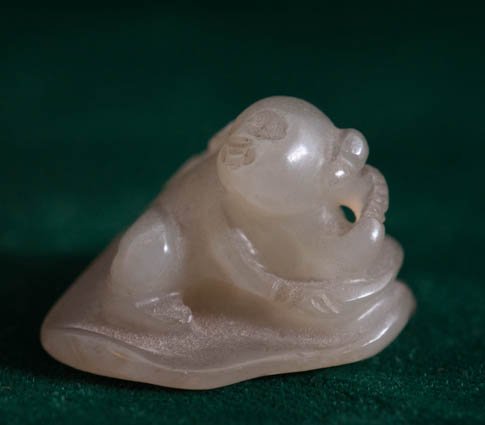 Small Jade Figure of Child: A white and brown jade carved figure of a child on a lotus flower, measures 1 1/8". Condition is good