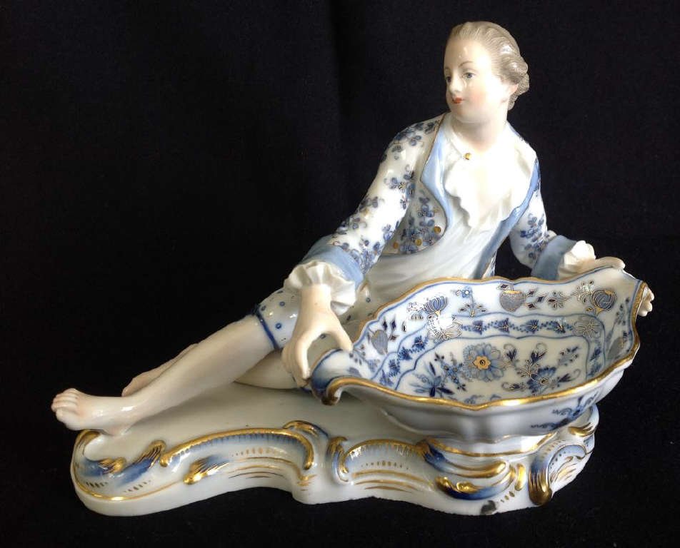 Early 20th C Meissen Figural Sweetmeat: blue and white barefoot man reclining by onion pattern painted bowl with gilt rim. Crossed swords mark.