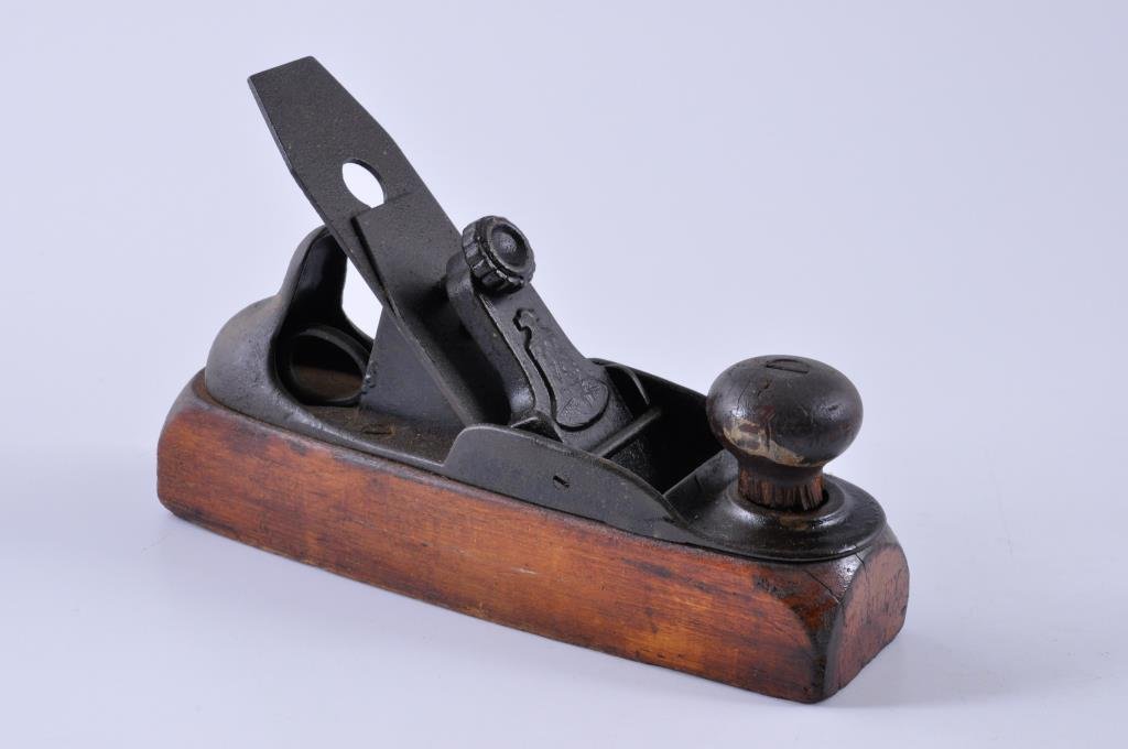 Stanley Wood Bottom #122 Plane with a Liberty Bel: 8” x 2” Stanley #122 Plane, made circa 1876. The front knob has significant chips along the base, and there is a crack in the sole. Condition: fair