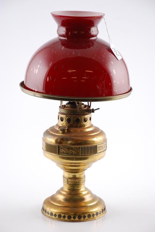 Edward Miller Co. Brass Fluid Table Lamp: Edward Miller Co. Embossed and Reticulated Brass Fluid Table Lamp. Burgundy cased shade. Condition: Several dents along or near reservoir band. Tarnish and wear to brass. Unevenness and minor crack to