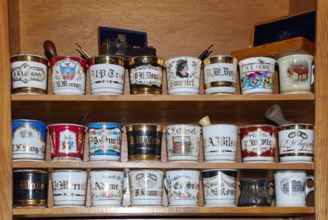 Collection of 19thc Personalized Shaving Mugs Etc.: (23) Ceramic shaving mugs, straight edge razors, a cased set of Wilkinson razors and a personalized cased set of (7) Mappin & Webb London straight edge razors for each day of the week. Condition: Good