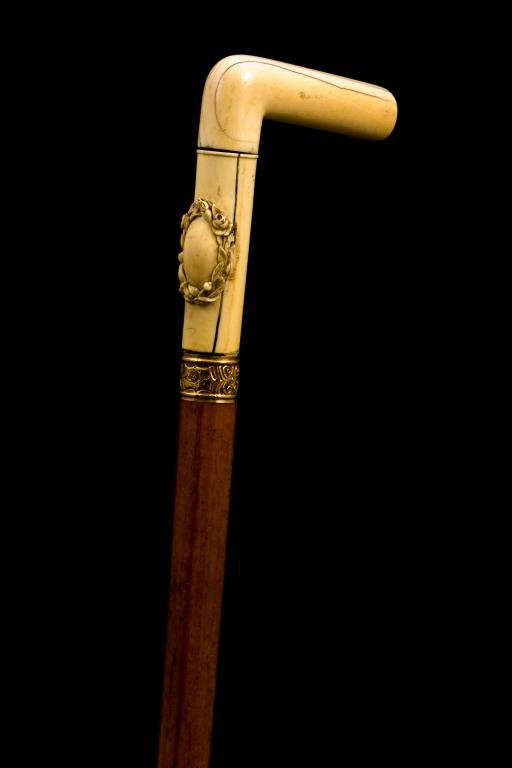 "L" HANDLED CANE CARVED WITH WREATH OF FLOWERS: Circa 1890, 4 x 4 1/2 inch two-piece carved handle, unmarked gold embossed collar, fine burl wood shaft with horn ferrule. Length 35 inches