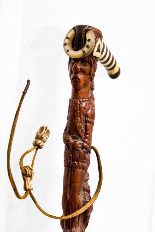 PACIFIC NORTHWEST THEMED CANE WITH FRONTIERSMAN: 3 1/2 inch bird-form crop handle is comprised of concentric rings of bone and horn and is capped with metal tip. Silver and bone inlays and an abalone horseshoe complete the handle. A shaft of exotic 