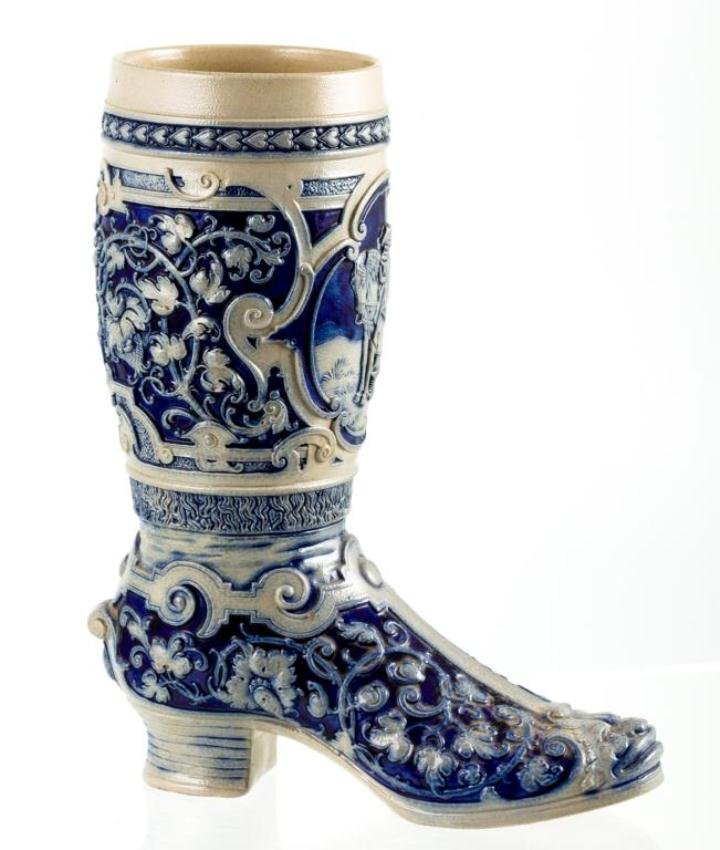 SALT GLAZED COBALT STEIN IN THE FORM OF A BOOT: All-over floral pattern with vignette of a cavalier blowing a bugle. Height 11 1/4 inches