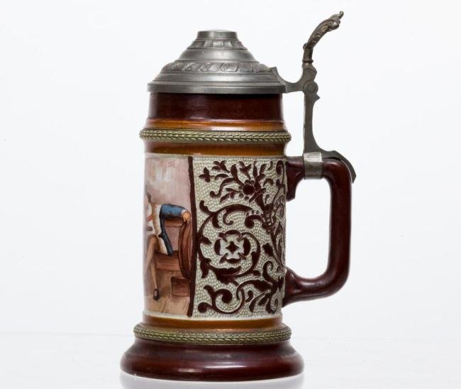 HAND PAINTED STEIN SIGNED "HR GERMANY" 1/2 L: Green needle bands bracket a hand painted panel of a tavern scene as well as a relief floral pattern on a shagreen ground. Pewter lid. Height 8 1/2 inches