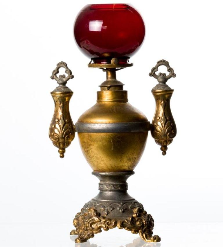 SMOKING PARLOR CIGAR LIGHTER WITH RUBY SHADE: Ratchet Union kerosene lamp with gold wash white metal font, double wire pipe cleaners, blown molded ruby globe with 2 inch fitter and round rococo footed base. Height 10 1/2 inches