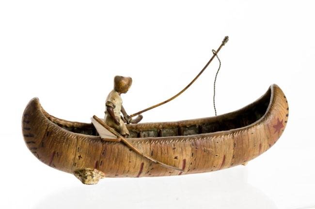 BLACK AMERICA CAST METAL FISHERMAN IN CANOE: Hand painted cast metal fisherman in a birch bark canoe. The fisherman's line is caught under rock or log. Length 9 inches