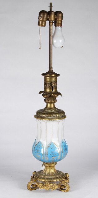(19th/20th c.) Blue Cut to Milk Glass Lamp: Gold highlighted cut glass lamp with finely cast ormolu mounted floral base, gadrooned egg and dart collar and leaf motif stem. Height to fitter 18 inches. unmarked. Condition: Converted to electricit