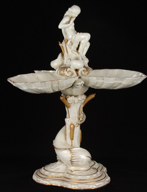 Gilt Porcelain Figural Centerpiece with Nude: Dolphin fish is wrapping reeds and cat o' nine tails which support (3) scallop shell dishes and nude who is surrounded by shells and snake. Height 18 inches. Condition: Good, (2) small chips to (1) sh