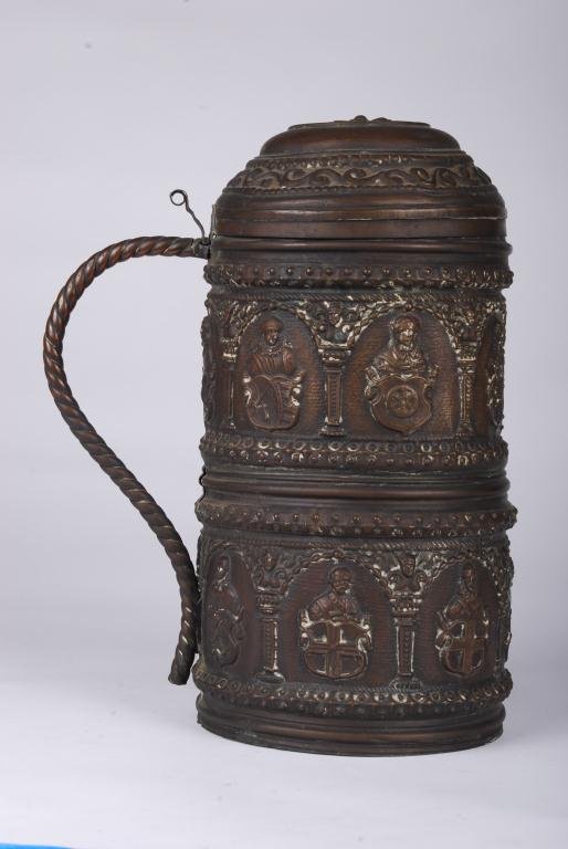 (19th c.) Brass Stein-Form Cannister: Decorated with embossed figures and coats of arms. Lead base. Height 11 inches. Condition: Surface grime