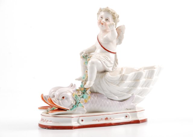 KPM Porcelain Cherub Riding Dolphins: Outstretched arm holding note. height 7 1/2 inches. signed. Condition: Note broken but piece present,