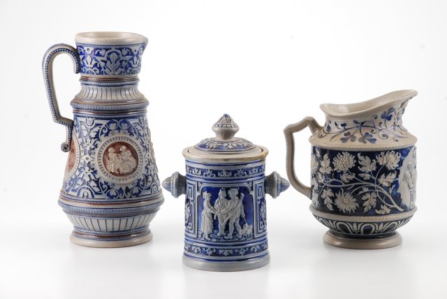 (3) Pieces of German Salt Glazed Stoneware: Including a pitcher marked Germany, height 9 inches, pitcher with medallions height 12 inches and a covered jar, height 8 inches. Condition: Good