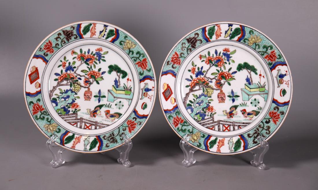 Pair Chinese Qing Famille Verte Porcelain Plates: Pair Famille Verte Enameled Porcelain Plates with a design of chickens under a flowering tree with a border of fish, games, and antiques between pairs of lotus. The reverse of each with an unidentifie