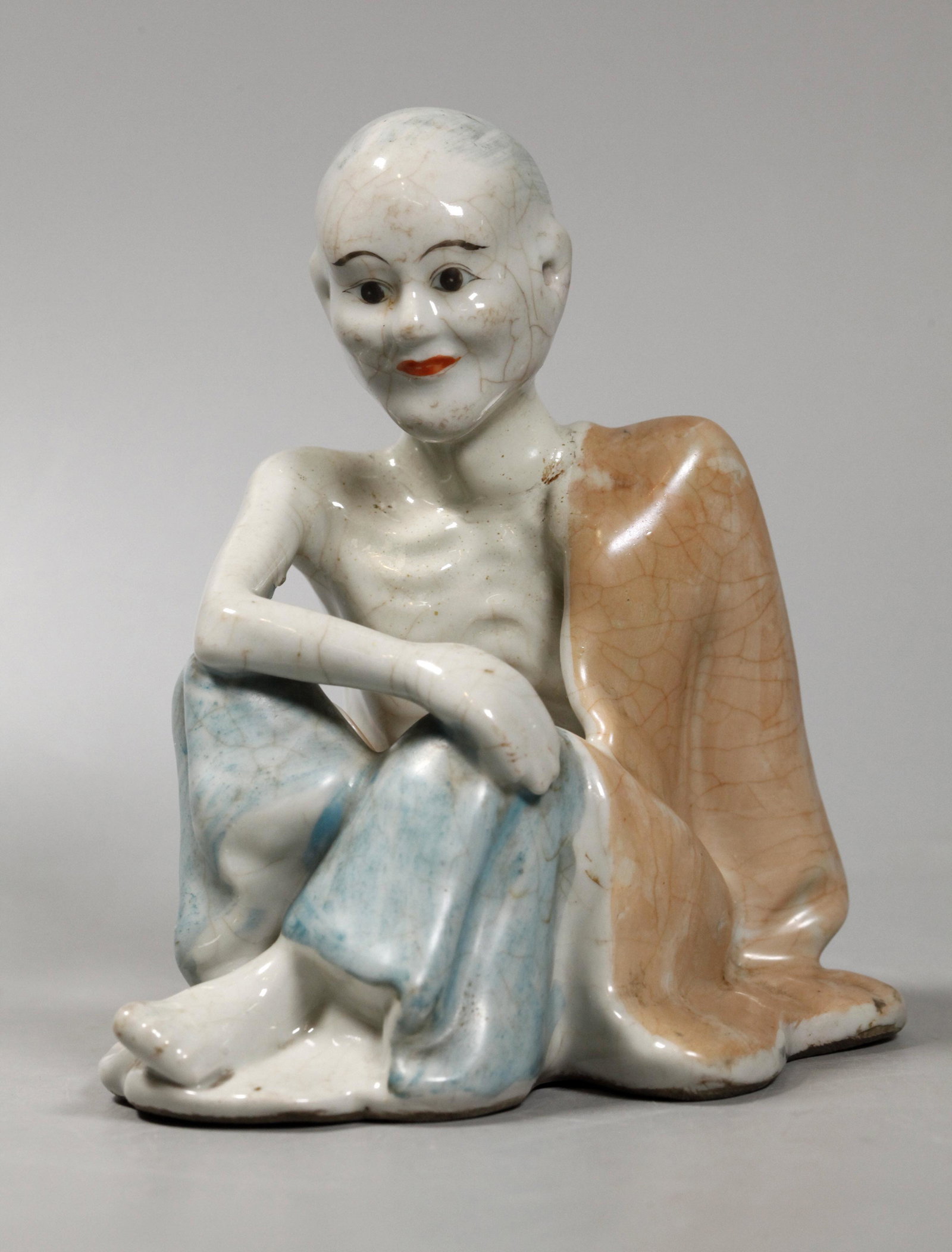 Chinese Enameled Porcelain Fasting Buddhist Lohan: Chinese Enameled Porcelain Fasting Buddhist Lohan seated with an orange robe. Age related wear with slight crackle to glaze, the head re-stuck with light over-painting. Height 6 1/2 inches (16.5 cm.).