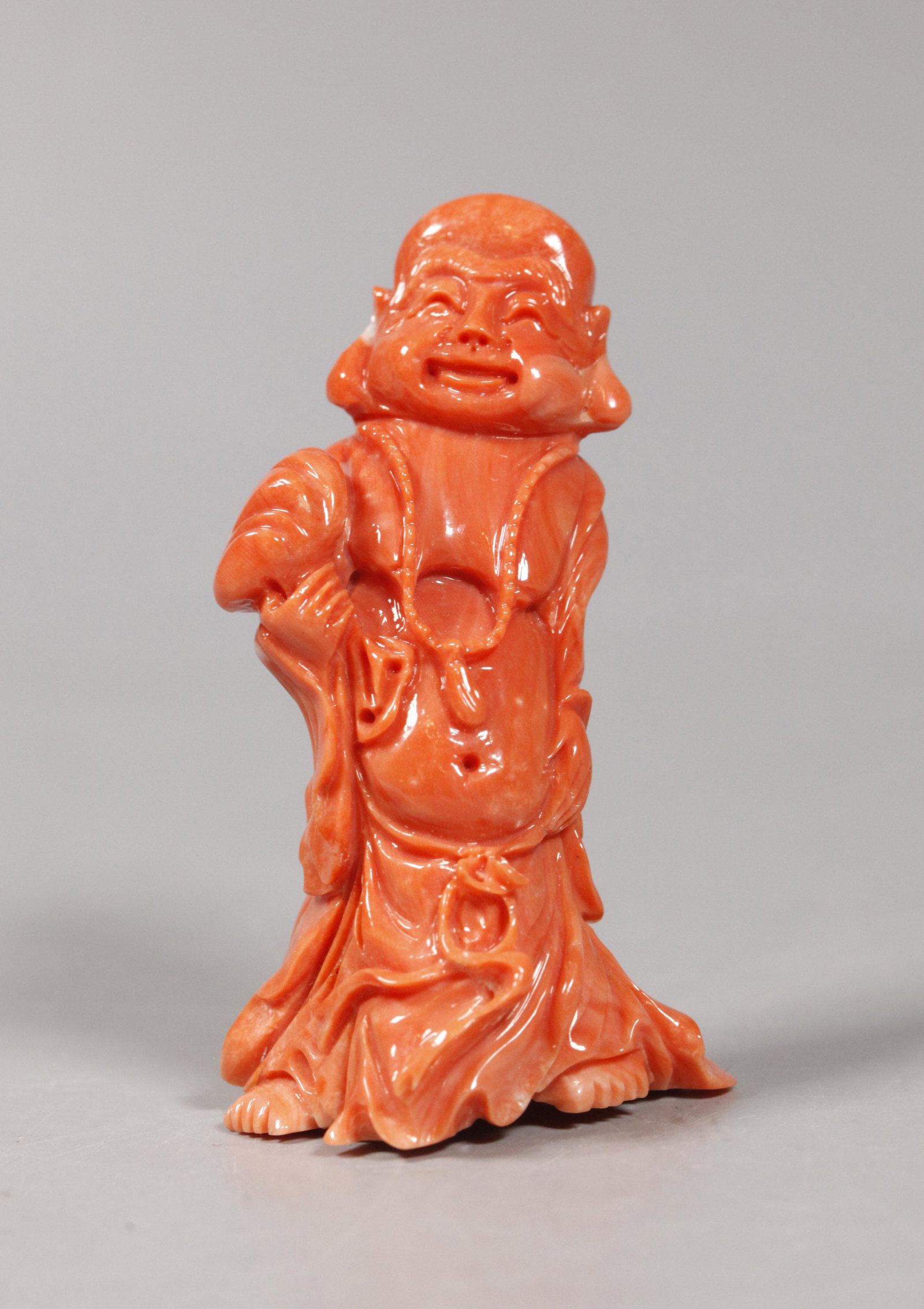 Chinese Carved Coral Bodhi Buddha; 60.8G: Chinese Carved and polished Coral Standing Bodhi Buddha with sack over right shoulder and wearing a Buddhist rosary around his neck. Good condition. Total weight 60.8 grams. Height 3 inches (7.6 cm.).
