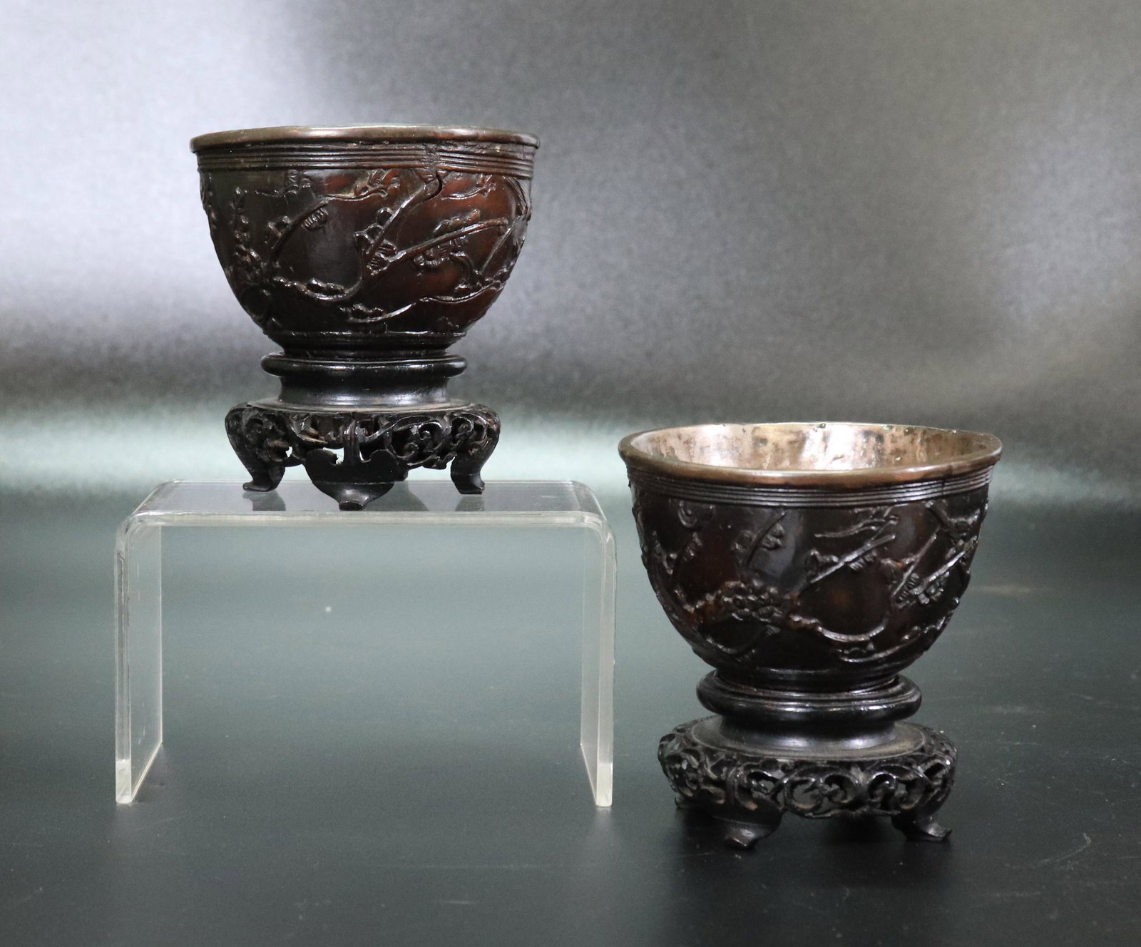 Chinese 18th/19th C Cocoanut Silver Wine Cups: Chinese 18th/19th Century Cocoanut Shell Wine Cups carved with Garden Scenes with flowering branches and lined in silver; with a pair of old pierced 4 footed antique hard wood stands. Height of cup 1 