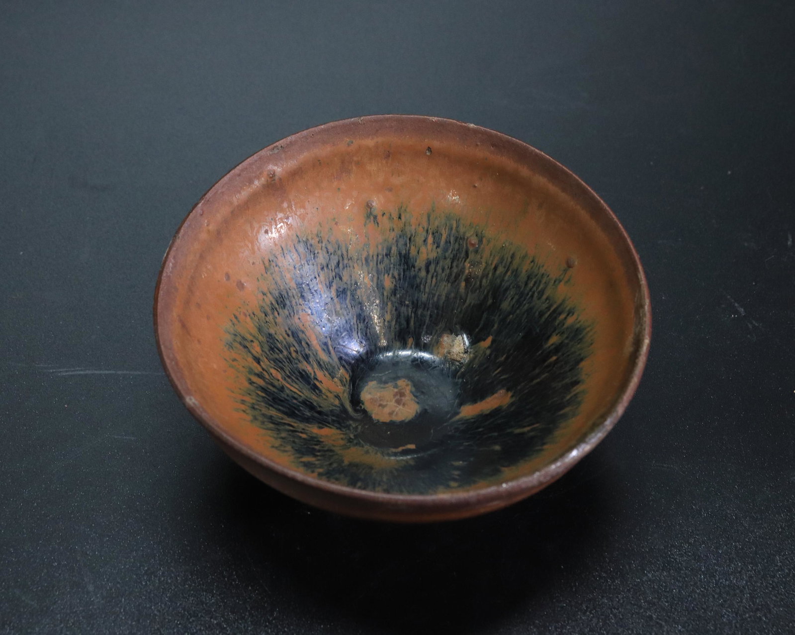 Chinese Jian Hare's Fur Glaze Teabowl: Chinese Jian Hare's Fur Glaze Teabowl, the thick glaze draining from the brick-brown mouth and forming a roll before the unglazed foot revealing the gray clay. Height 2 1/4 inches (5.5 cm.).
