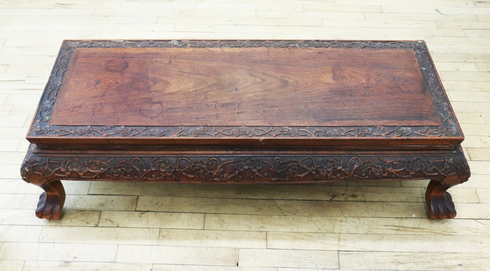 Chinese Carved Hard Wood Kang Table: Chinese Carved Hard Wood Kang Table with a panel top with cross supports underneath and bordered with stems of flowers carved in relief, the same design to the skirt under the top ending in 4 claw & b
