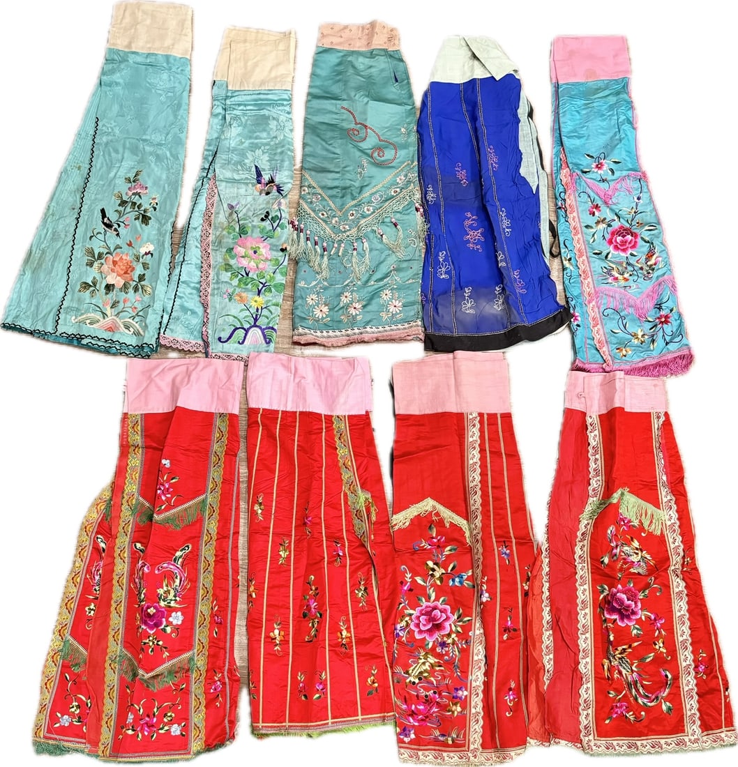 10 Chinese Embroidered Satin Skirts: 10 Chinese Embroidered Satin Skirts, in various colors, each with ribbon decorations, satin stitch embroidery and 1 with remains of knotted fringe. General Height 34 inches (86.5 cm.).