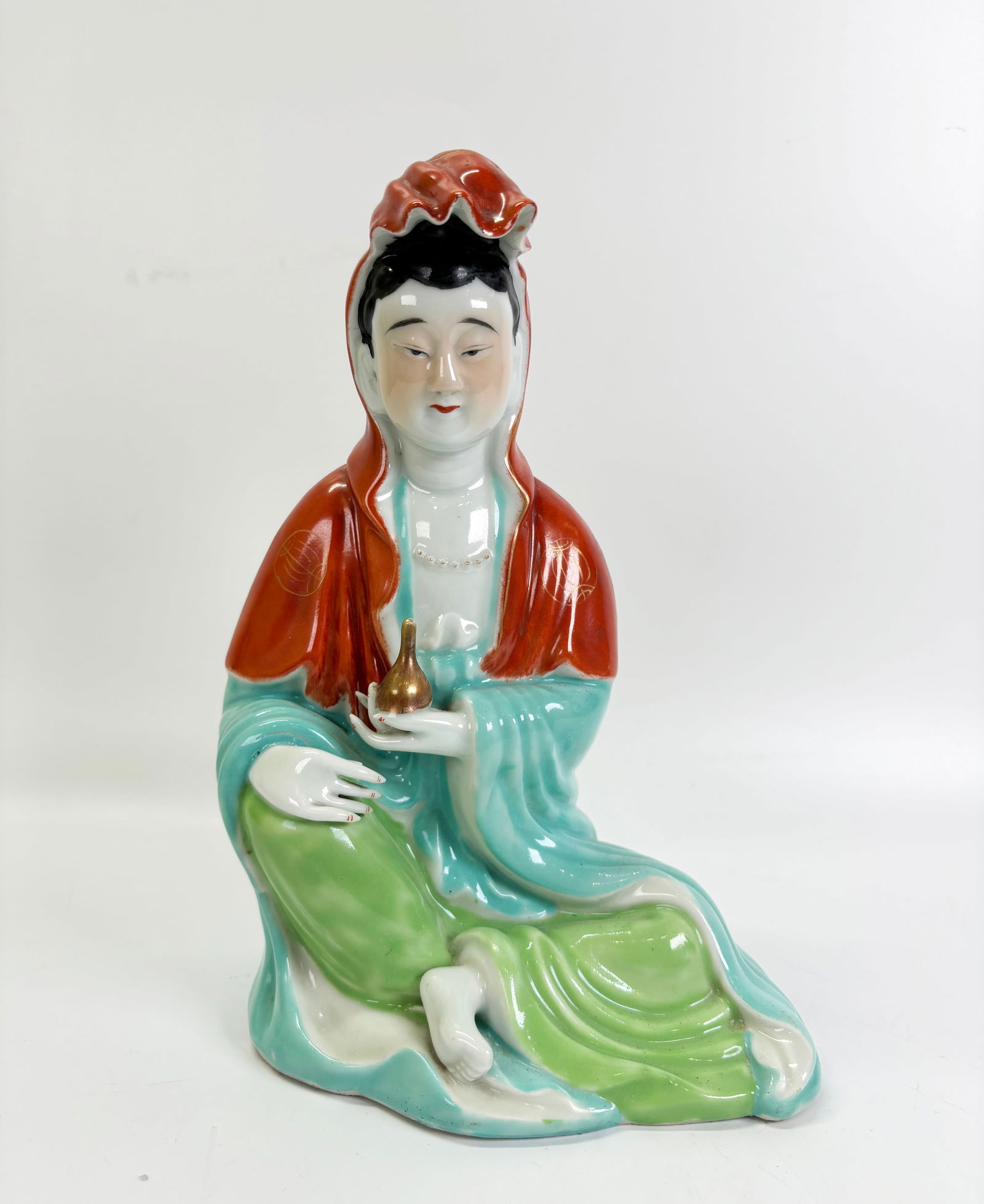 Chinese Enameled Porcelain Seated Guanyin Figure: Chinese Enameled Porcelain Seated Guanyin Figure in robes of iron red with gilding, turquoise and light green and holding a gilt vase of compassion; the flat base unglazed. Height 9 1/2 inches (24cm.)