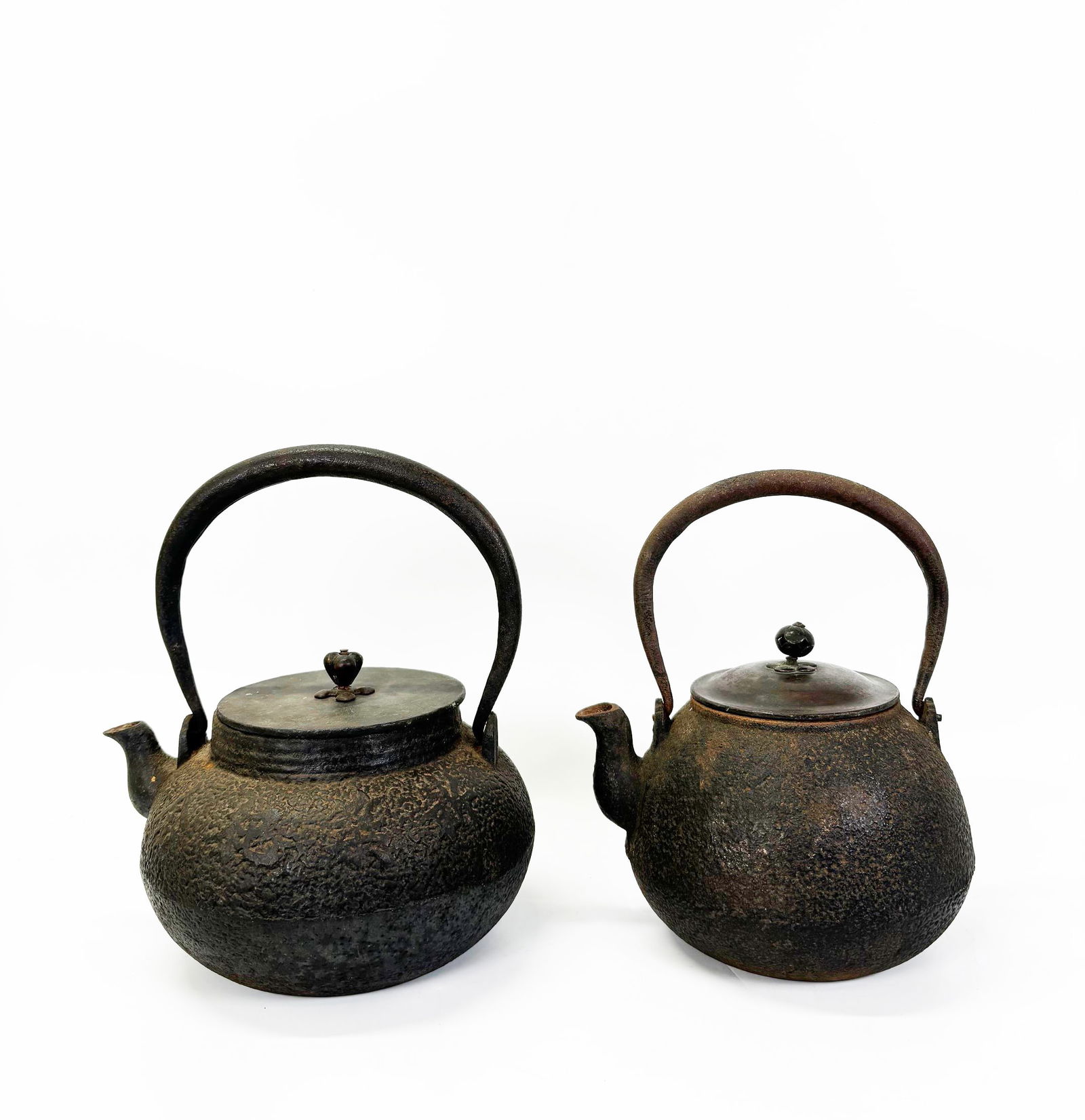 2 Japanese Tetsubin with Bronze Covers: 2 Antique Japanese cast iron Tetsubin with wrought overhead handles and Bronze Covers with swivel finials, the larger with a design of calligraphy to sides and a Mon to left of spout, the bronze cover