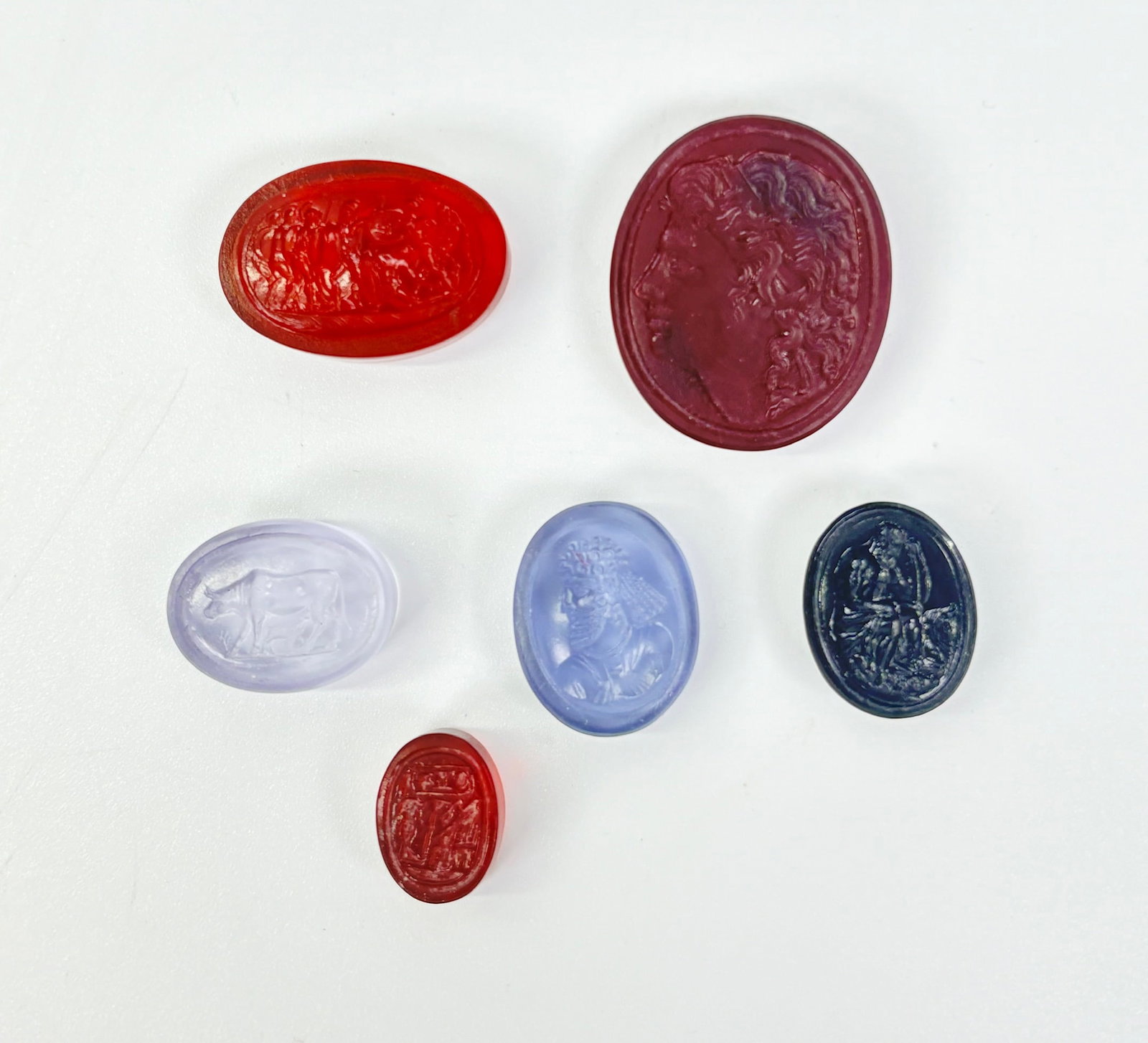 6 Tassie 18th/19th C Glass Paste Intaglio Gems: 6 James Tassie or Tassie-Type Glass Paste Intaglios, 18th/19th Century with polished backs and sides; the largest in ruby red glass with a neo-classical head in profile, an amber glass with muscular G