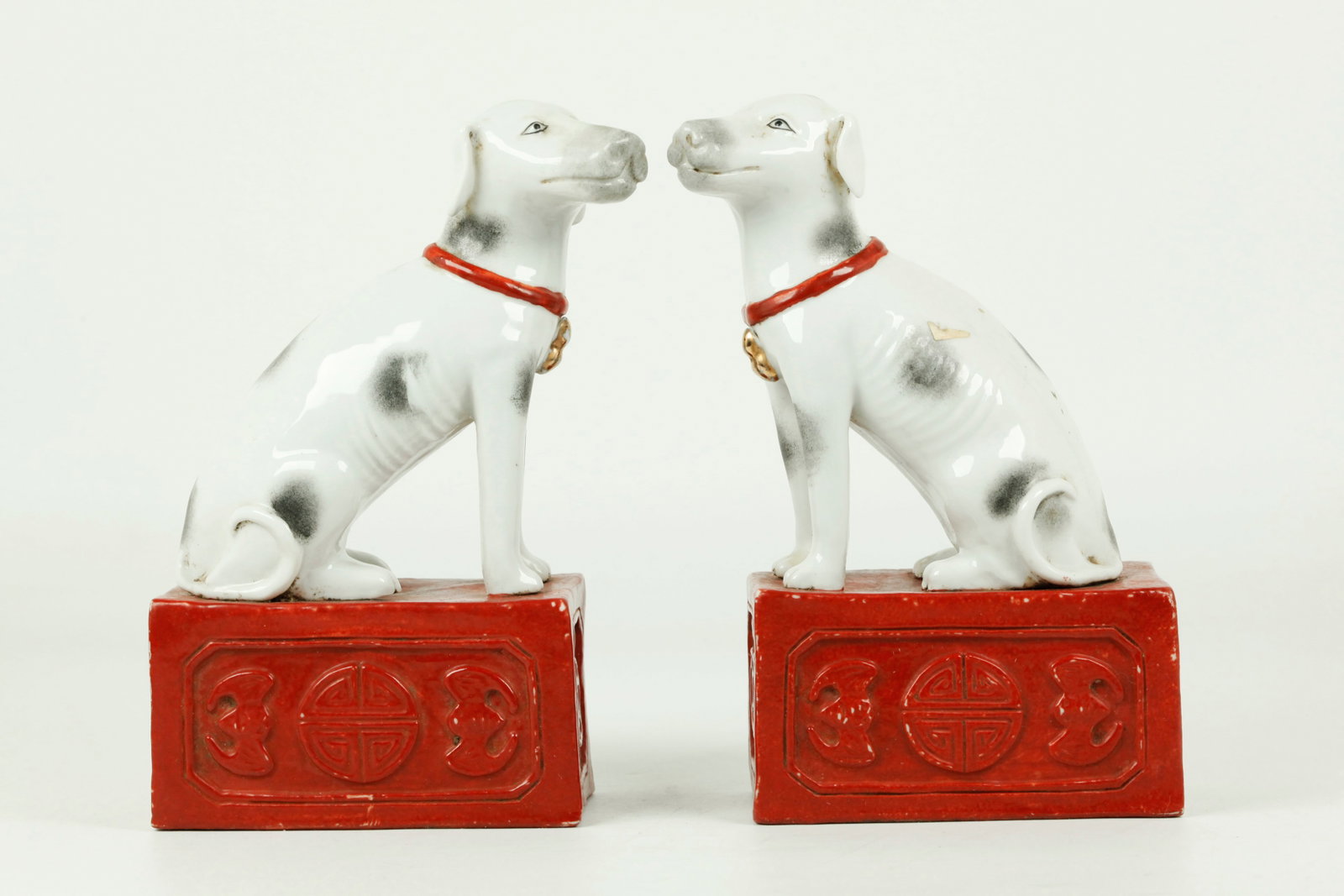 Pr Chinese Porcelain White Hounds Coral Bases: Mirror Pr Chinese Porcelain spotted White Hounds seated on Coral glazed Bases with Shou roundels, Bats and double Cash-Coin holes to ends; the unglazed flat bases with impressed seal marks. Height 7 i
