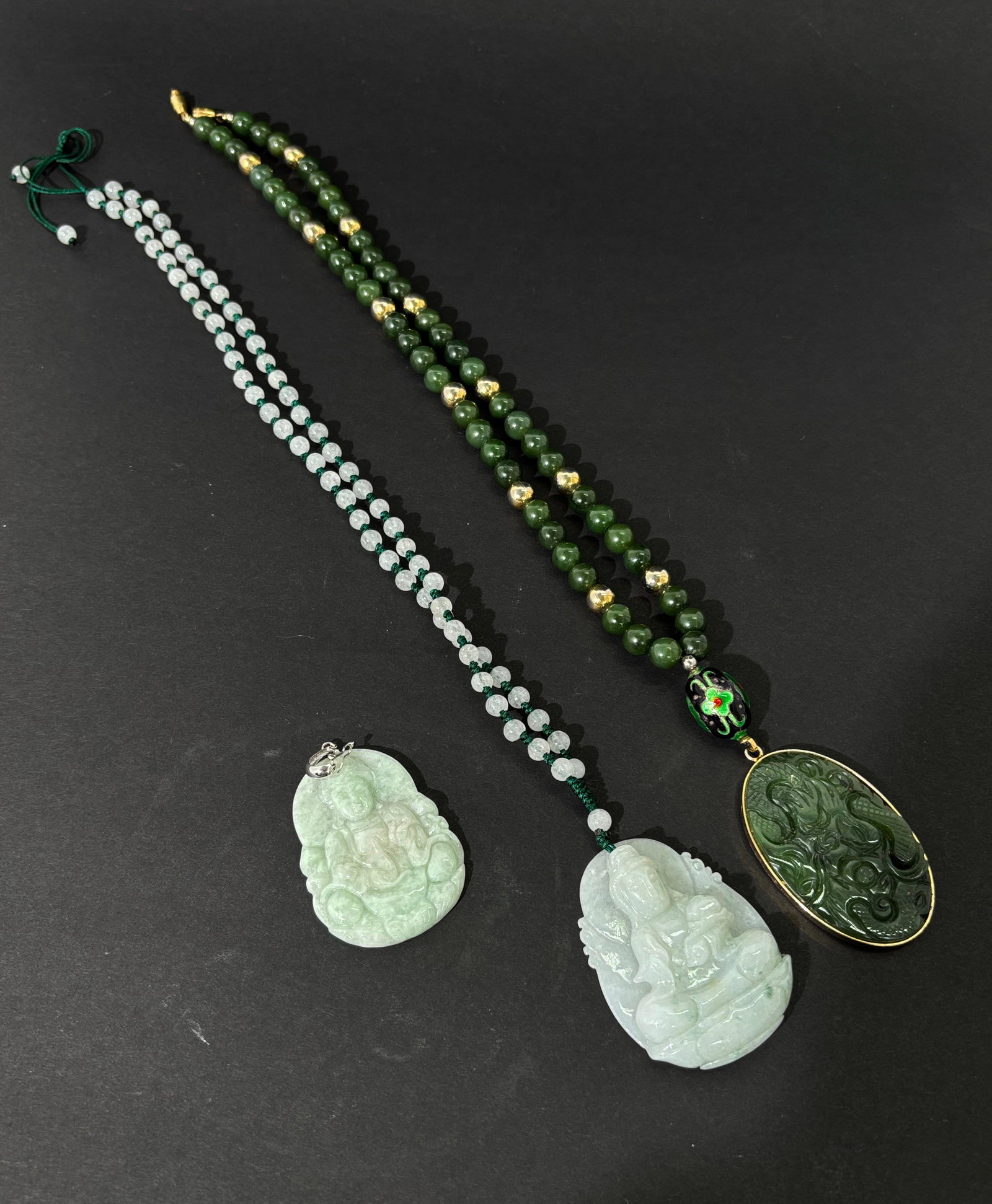 Two Chinese Jadeite Pendants, One Green Jade: Two Chinese pale celadon jadeite pendants carved with Guangyin, 1 with small bead necklace; together with a green jade bead necklace with Dragon carved oval pendant. Height of large pendant 2 1/8 inch