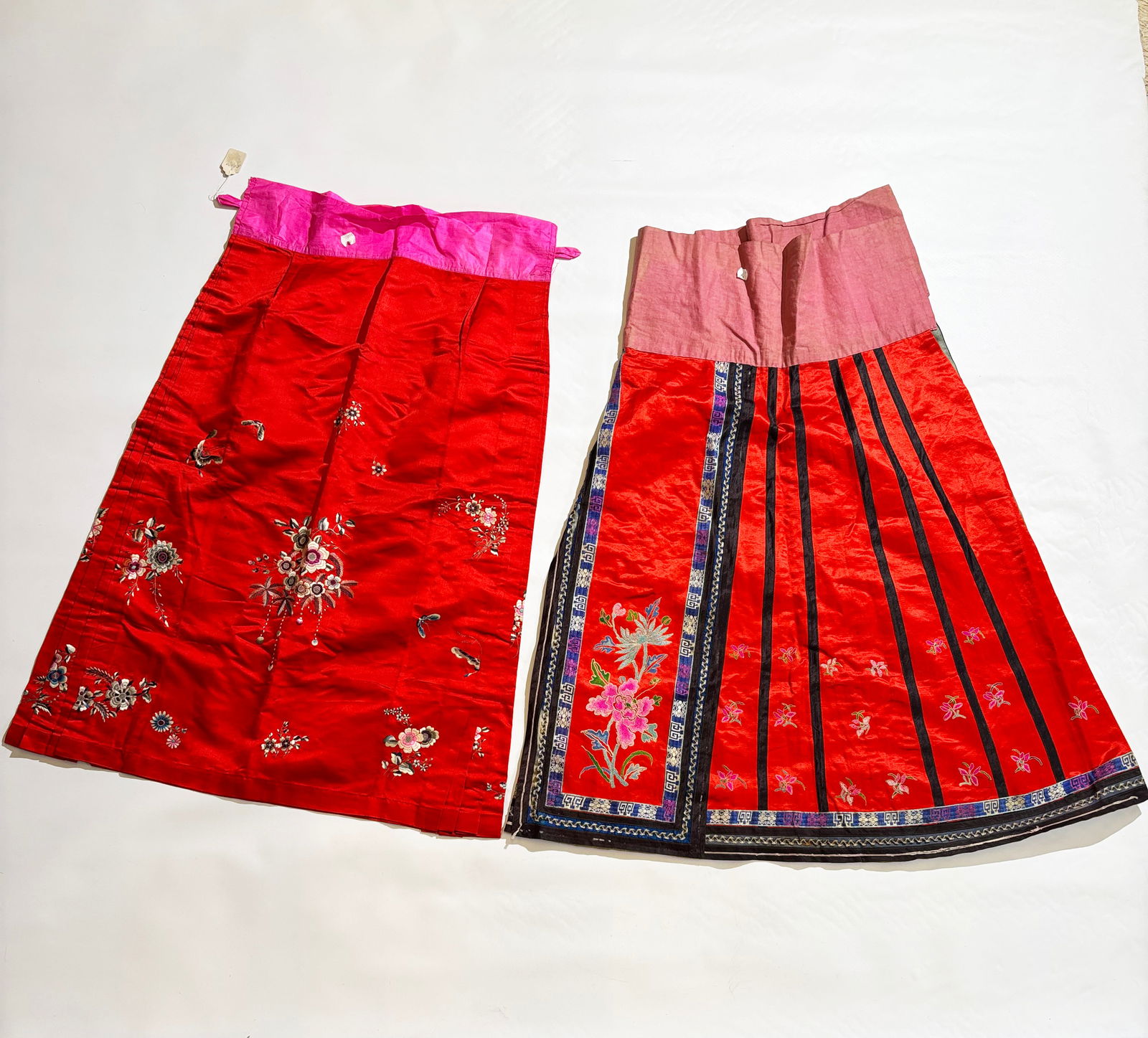 2 Chinese Qing Embroidered Red Satin Skirts: 2 Chinese Qing Embroidered Red Satin Skirts; 1 with folds sewn to the sides as a sheath and with scattered flowers in satin stitch with no lining; the other a wrap around with 2 loop stitched flower p
