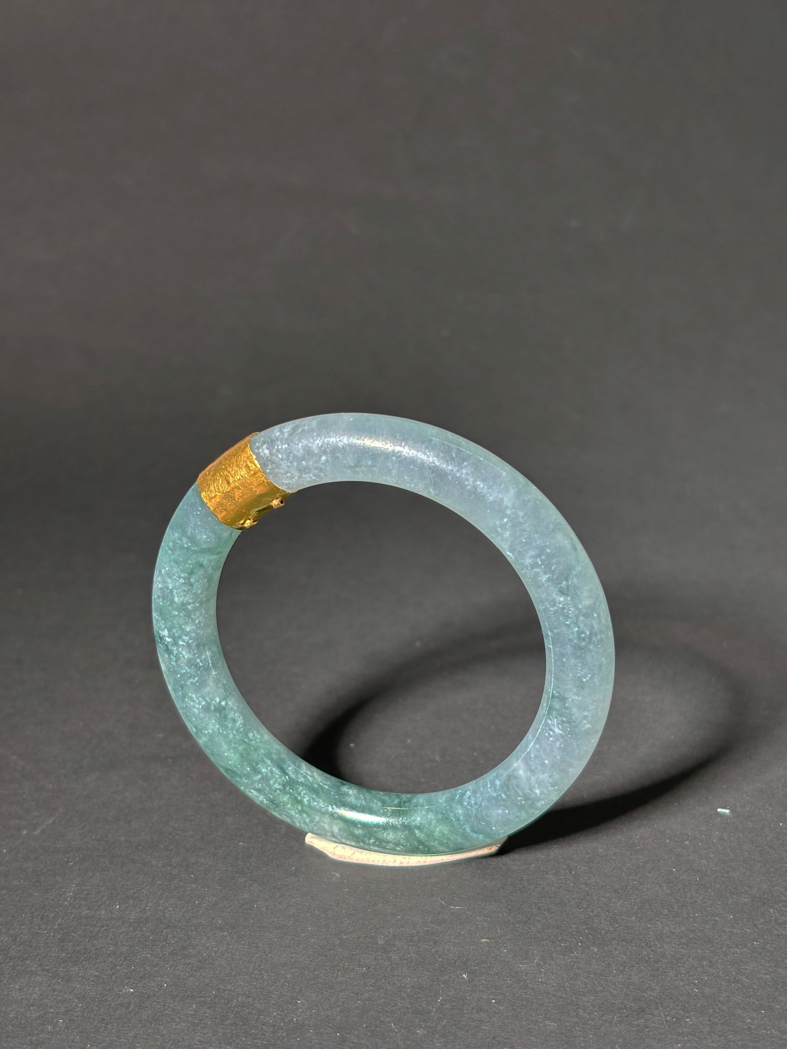Chinese Icy Clear & Green Jadeite Bangle Gold Band: Chinese translucent Icy Clear to dark Green Jadeite rounded Bangle decorated with 1 High Karat Yellow Gold Band fitted inside with 2 prongs. Diameter 84.6mm.