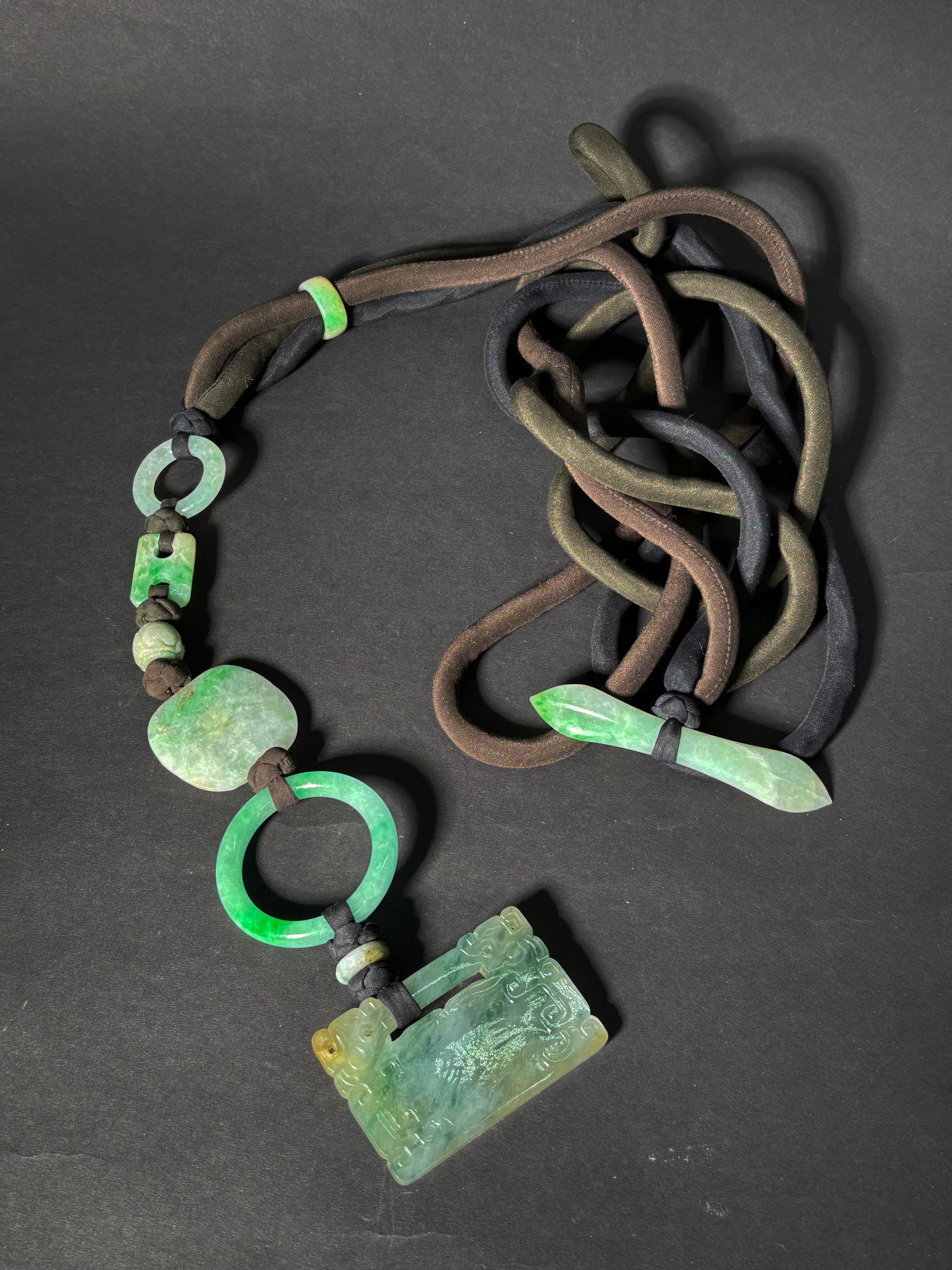 9 Chinese Pale & Green Jadeite Beads & Pendants: 9 Chinese Pale Green to Apple Green to Dark Green Jadeites: a Lock Pendant in translucent Icy pale celadon to dark green with touches of russet carved with confronting archaistic Dragon Heads at the c