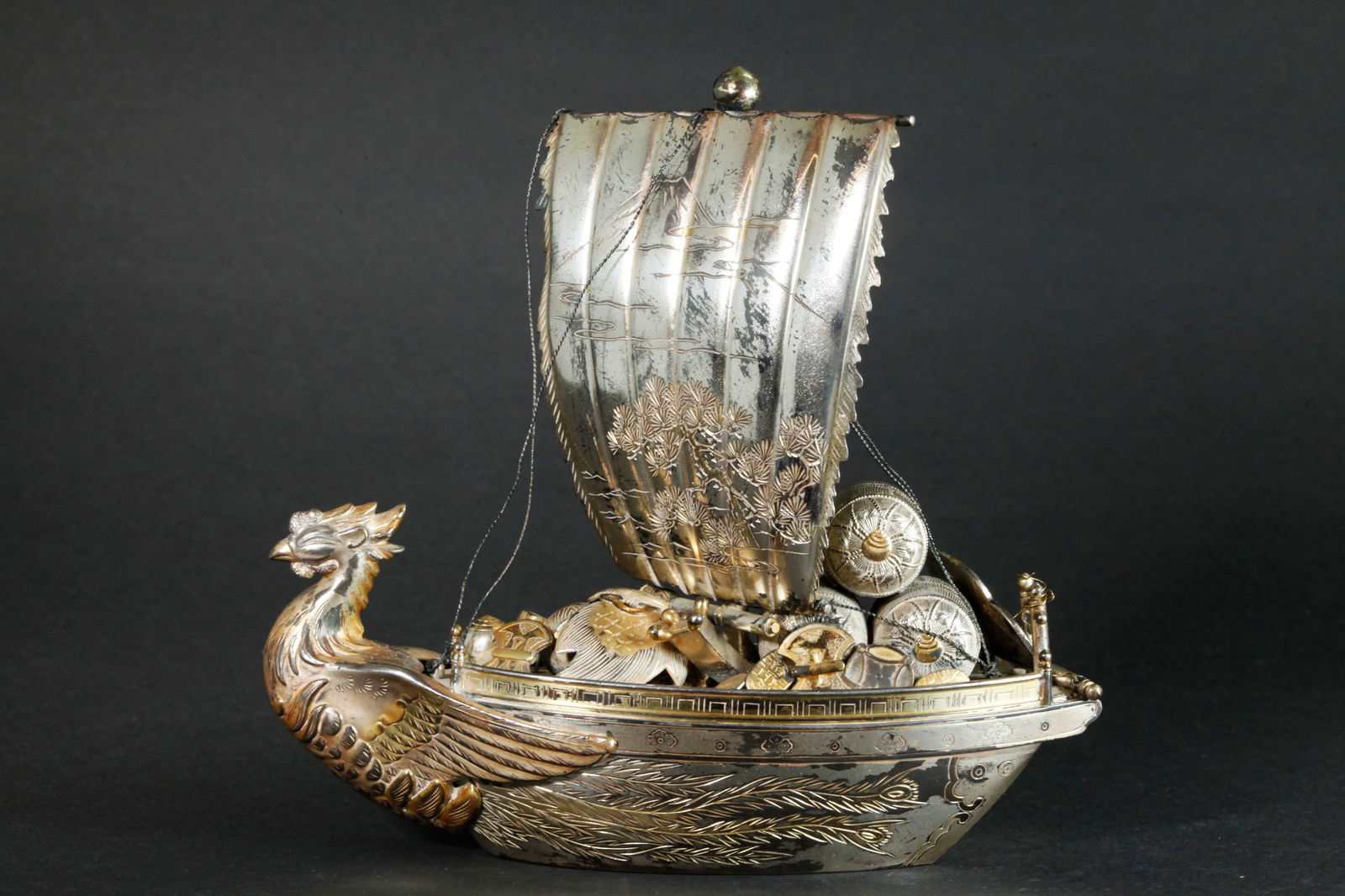 Miyamoto; Japanese Silver Marked Takarabune Ship: Japanese Silver "Takarabune" New Year's Treasure Ship part gilt with a Ho-o Bird Prow and detachable rudder (now wired to stern railing), the fringed sail incised with a Pine tree * Mount Fuji in the