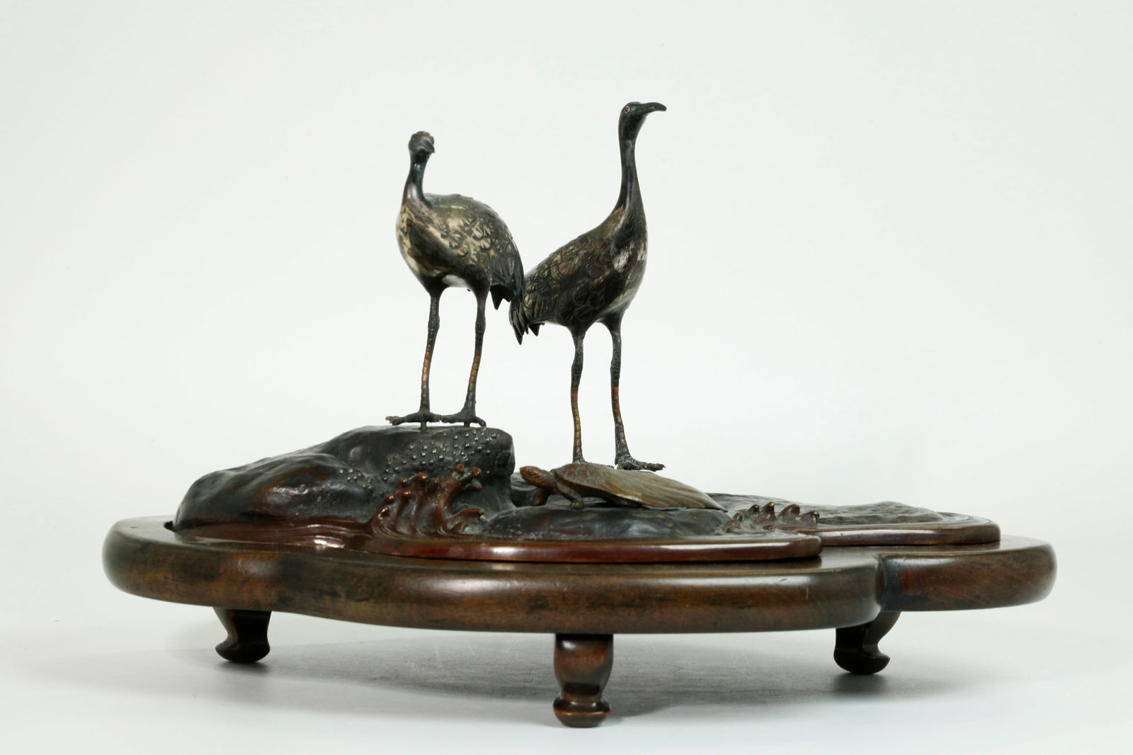 Seij Saku; Japanese Bronze Okimono Cranes & Turtle: Japanese silvered & patinated Bronze Okimono with wood stand on 3 curled feet, in a design of a pair of red crowned Cranes silver coated and mounted on blackened bronze rocks at the shore with a "Mino