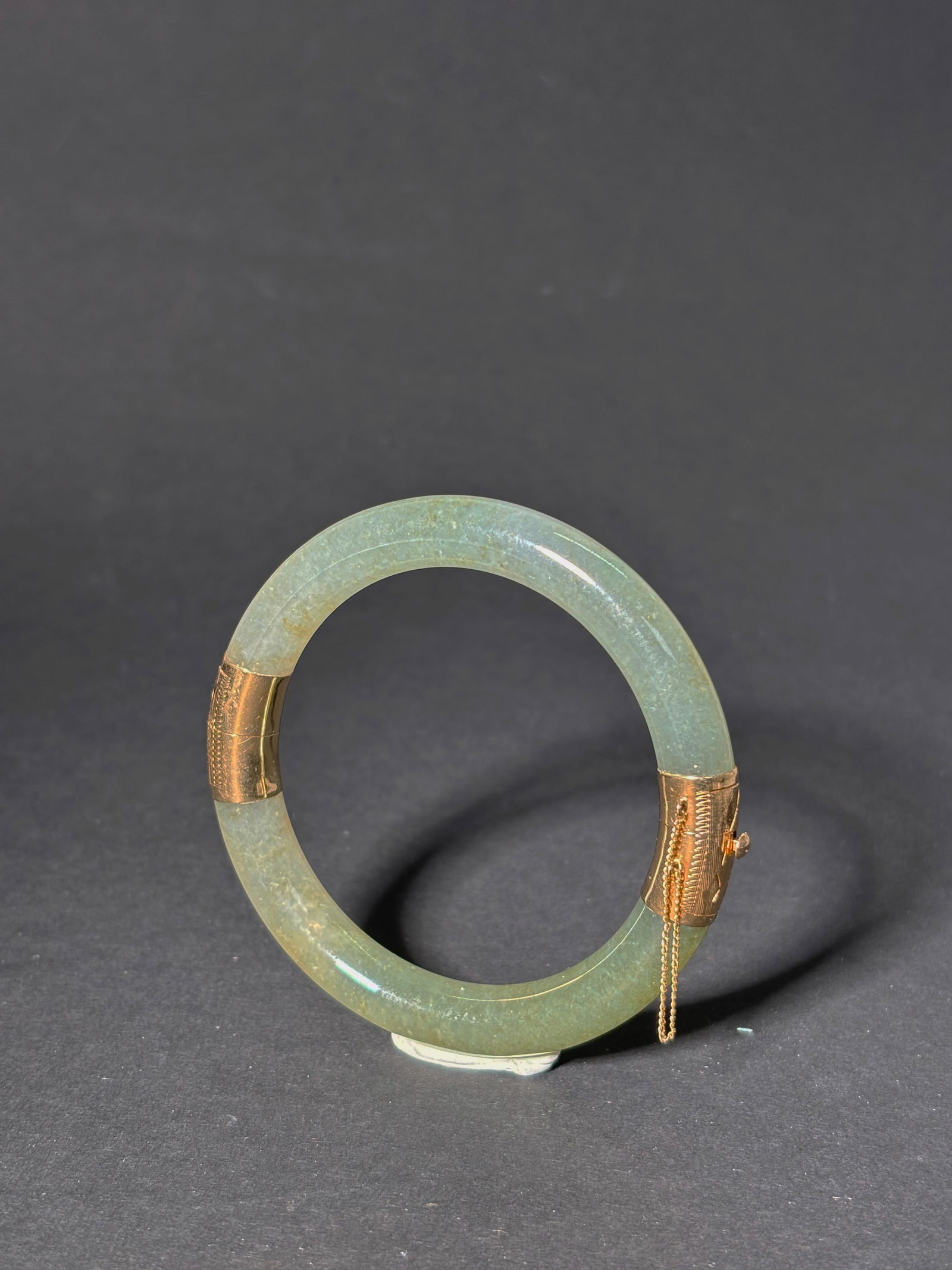 Chinese 14K Gold Hinged Icy Green Jadeite Bangle: Chinese 14K Yellow Gold Hinged, translucent Icy, pale Green Jadeite rounded Bangle, the closure with safety chain marked "14K / 585." Diameter 79.76mm.