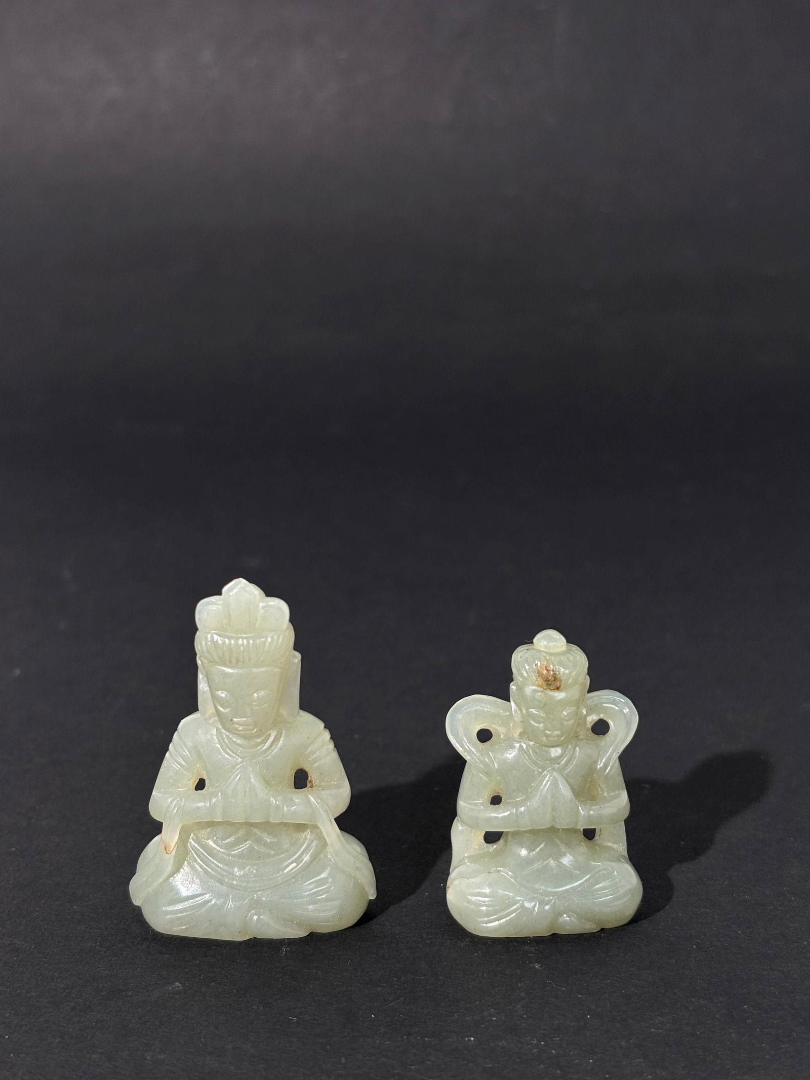 2 Chinese Pale Celadon Jade Seated Buddhas: 2 Chinese Pale Celadon Jade Seated Buddhas, both with hands in Anjali Mudra, the larger with a scarf across his arms and the smaller with a scarf lifted away from his shoulders; both flattened to stan