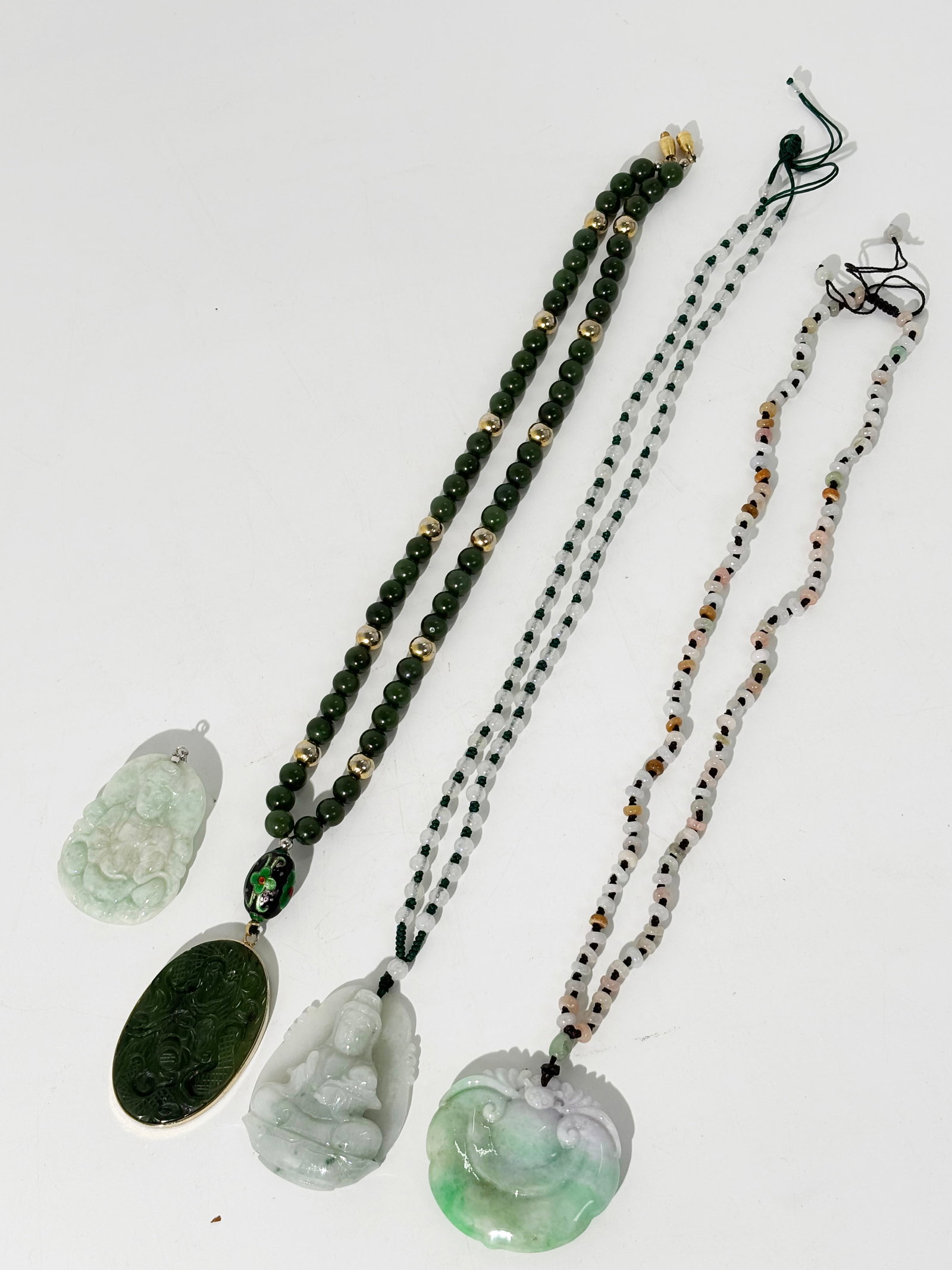 Three Chinese Jadeite Pendants, One Green Jade: Two Chinese pale celadon jadeite pendants carved with Guangyin, 1 with small bead necklace; together with a green jade bead necklace with Dragon carved oval pendant. Height of large pendant 2 1/8 inch