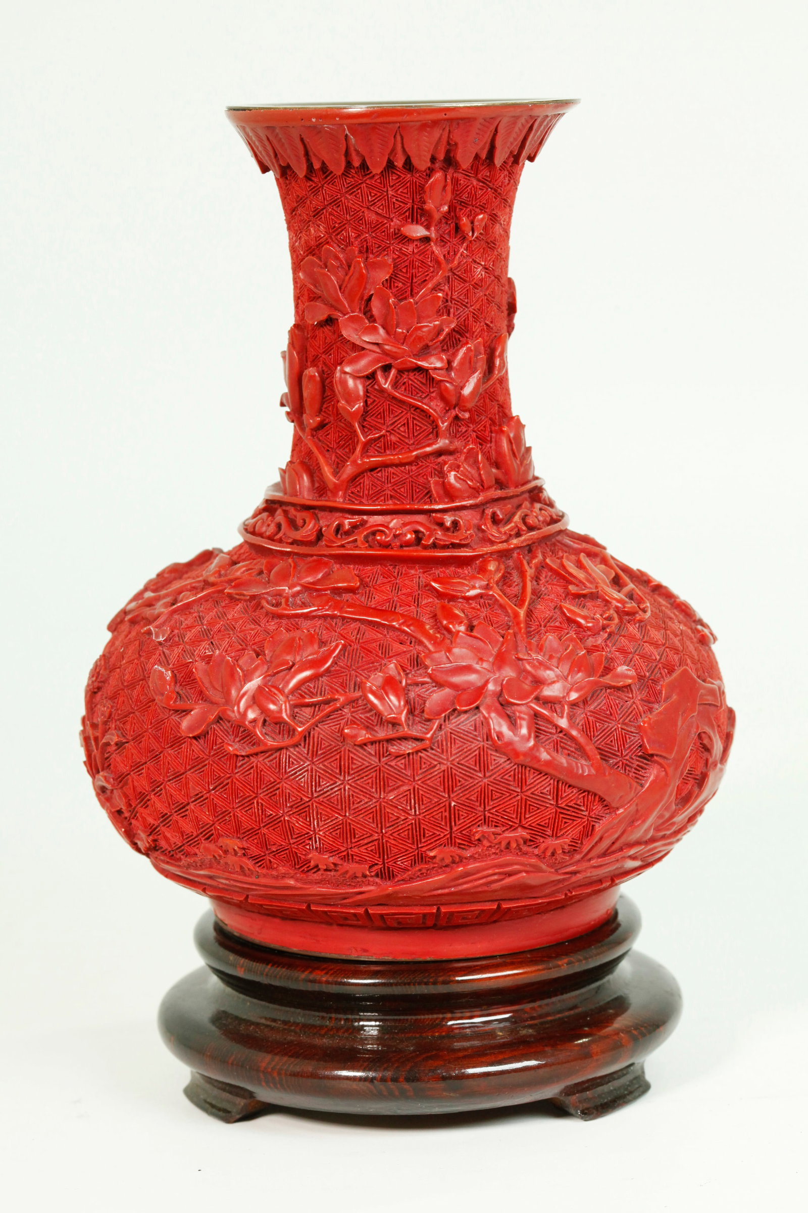 Chinese Cinnabar Red Composition Vase: Chinese Cinnabar Red Composition Vase molded with birds, flowers, branches and garden rocks on a brocade ground, the mouth with a bronze insert; with wood stand. Height of vase 6 3/4 inches X diameter