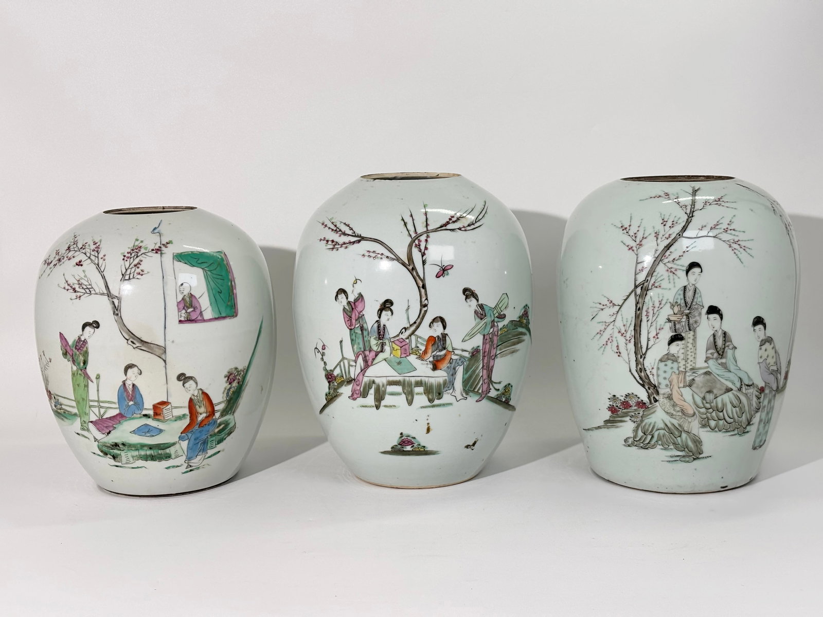 Three Chinese Famille Rose Porcelain Jars: Chinese export Famille Rose porcelain jars, each decorated with polychrome enamels in a figural garden scene. The hand-painted decoration depicts groups of women with trees and architectural elements,