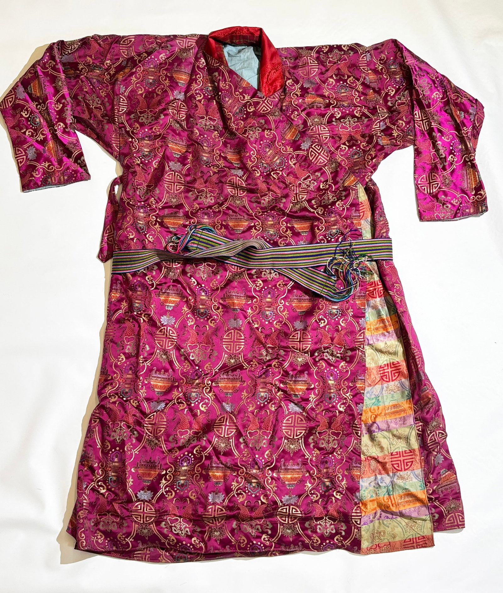 Tibetan Purple Silk Brocade Auspicious Object Robe: Tibetan Purple Silk Brocade Auspicious Object Design Robe with tie closures and turquoise cotton lining edged in red damask, with multi colored woven ribbon belt with fringe. Height 53 inches X width 
