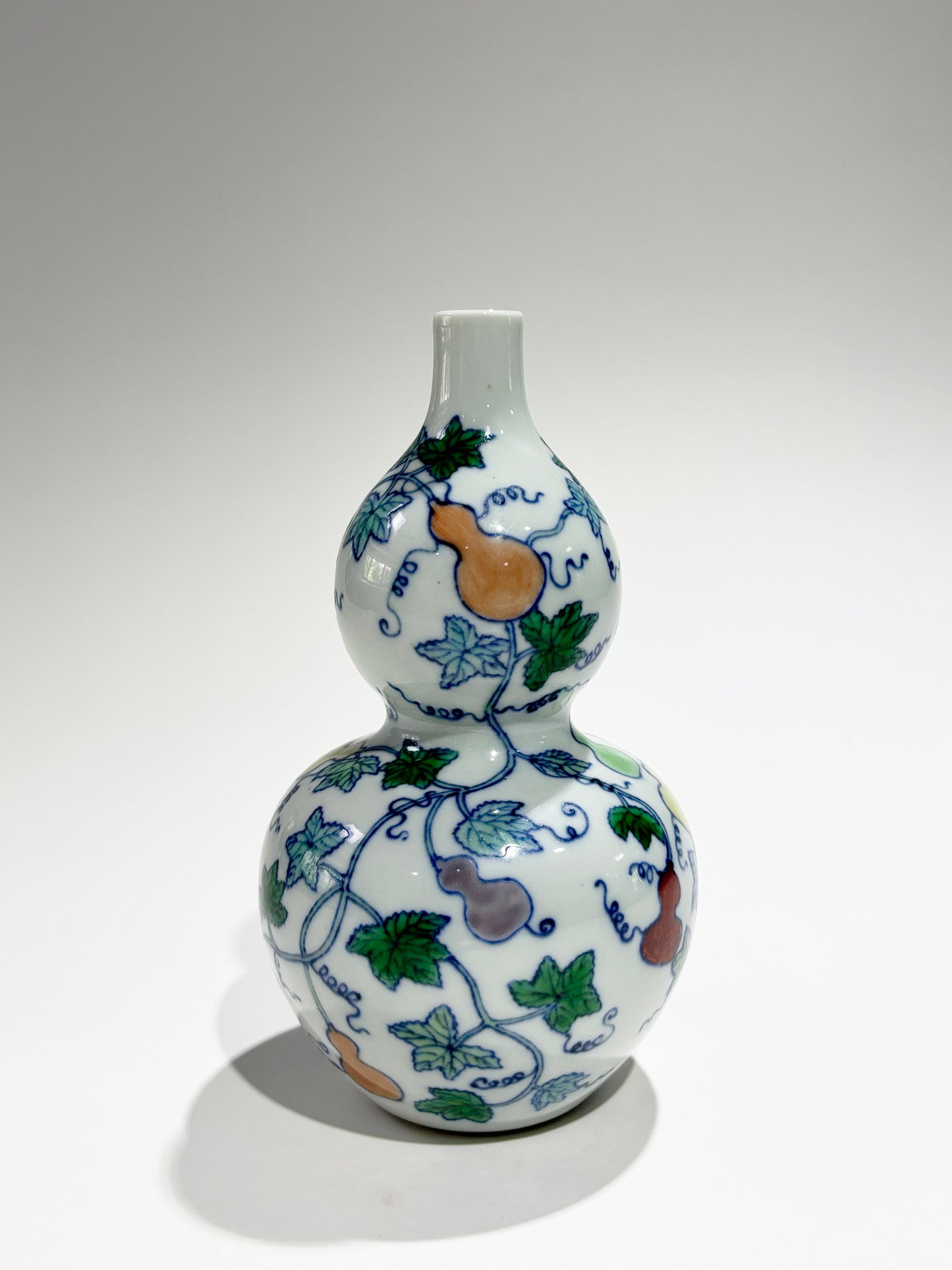 Chinese Doucai Enamel Porcelain Double Gourd Vase: Chinese Doucai Enamel over underglaze blue Porcelain Double Gourd Vase with a design of double gourds on vines with leaves & tendrils, the recessed base unglazed. Height 7 1/2 inches X diameter 3 3/4 