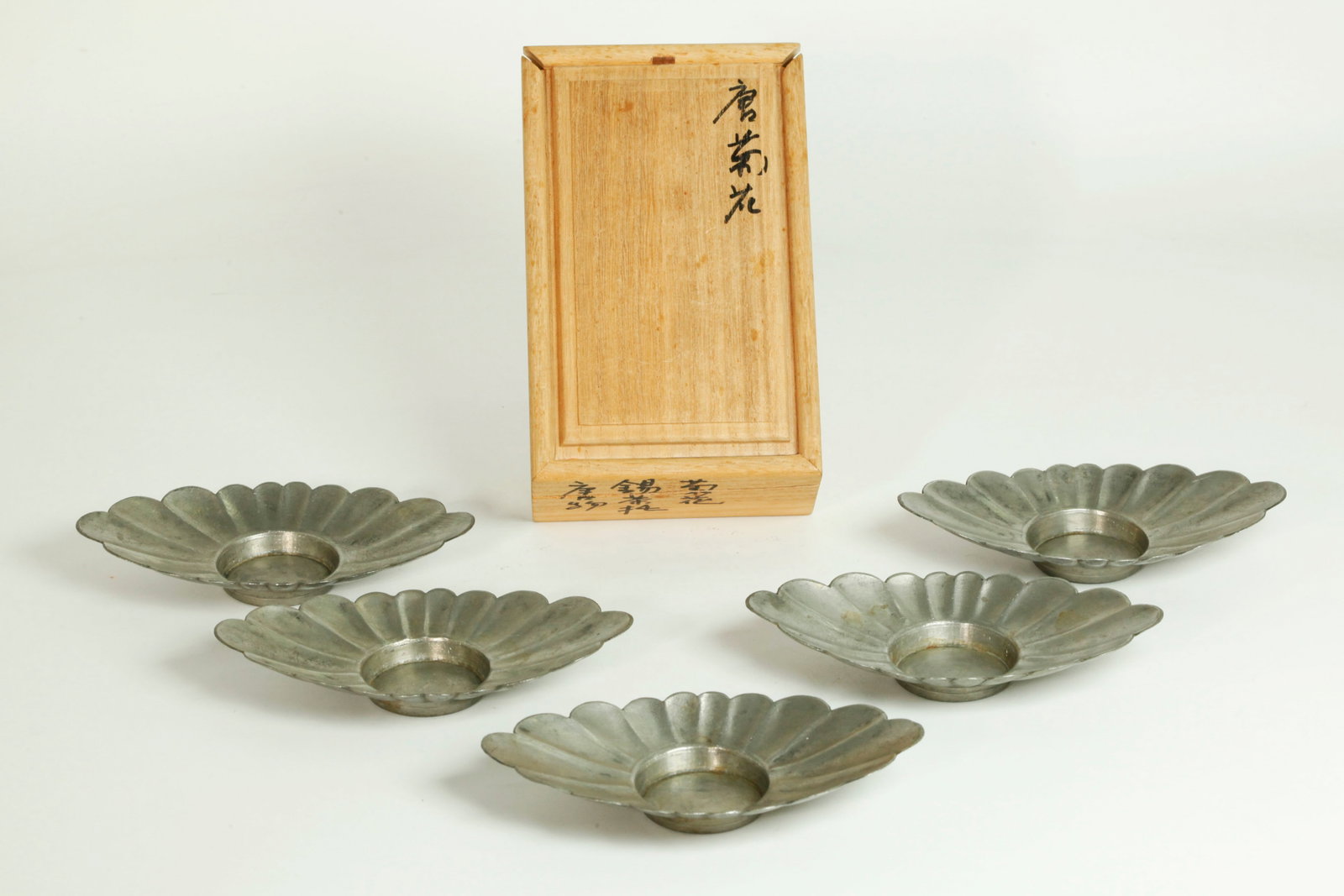 5 Chinese Qing Pewter Petal-Fluted Cup Stands: 5 Chinese Qing Dynasty Pewter Petal-Fluted Ovoid Cup Stands, each flat base impressed with a seal mark; wood storage box with ink inscriptions. Width of cup stands 5 5/8 inches X height 7/8 inch.