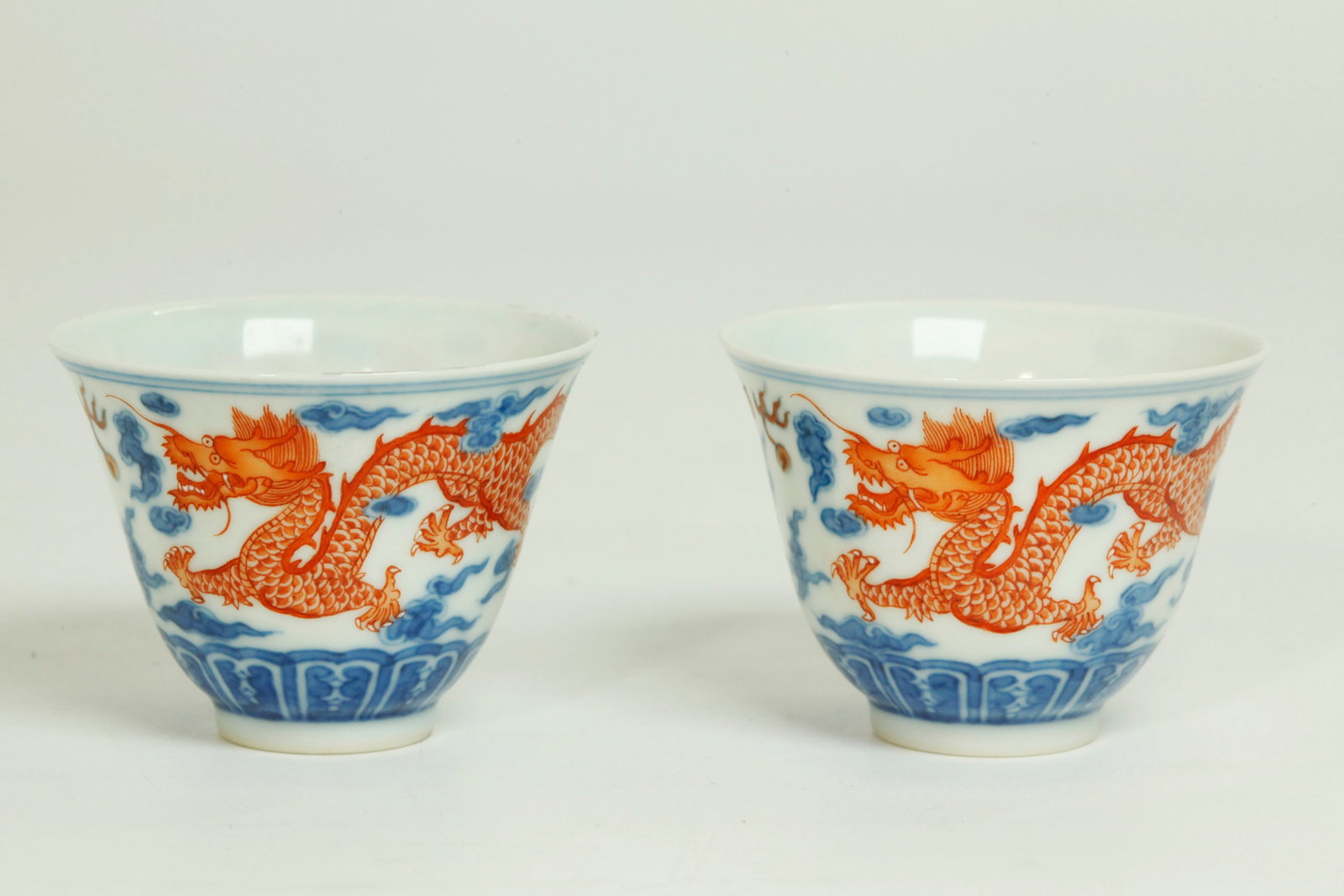 Pr Chinese 19C Blue Iron Red Porcelain Dragon Cups: Pair Chinese 19th Century underglaze Blue and Iron Red Porcelain Cups with a pair of 5-claw Dragons with white enamel teeth and claws between Flaming Pearls in Clouds, clear glazed inside at to recess