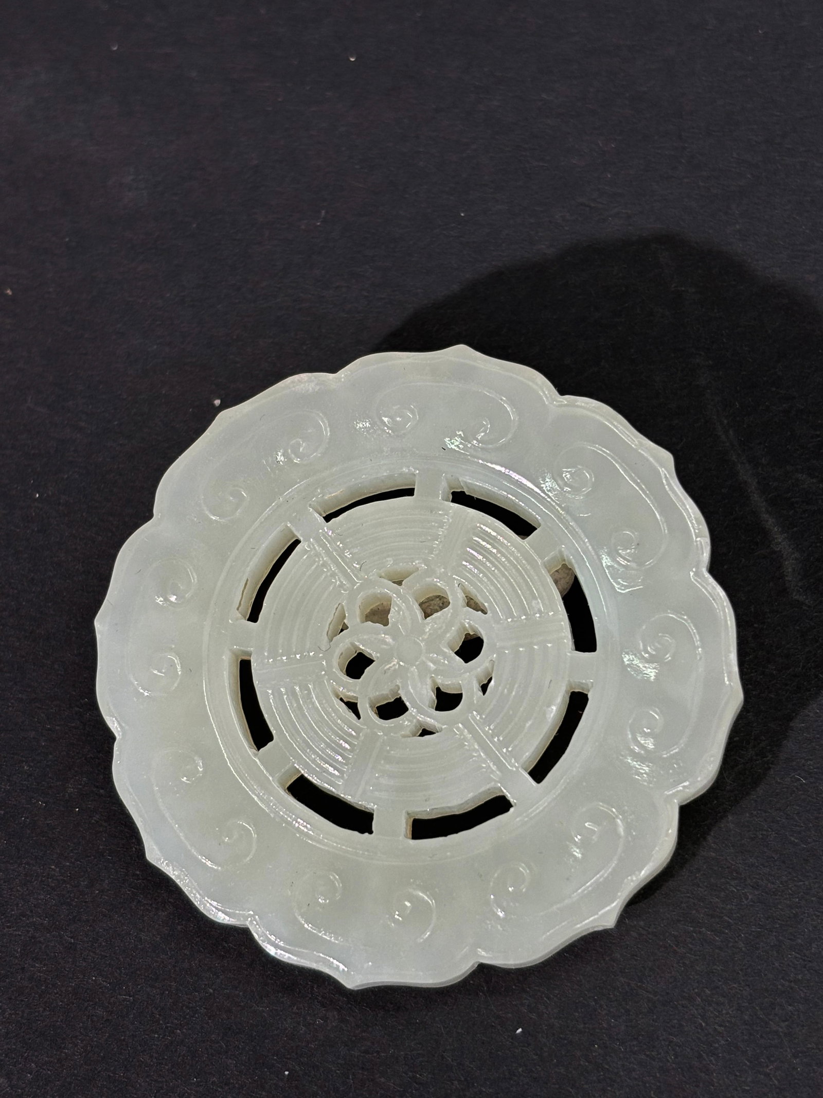 Chinese White Jade Wheel Disk Pendant: Chinese White Jade Wheel Disk Pendant with an outside border of Ruyi Heads around the Buddhist Wheel center pierced for suspension. Diameter 2 inches X approximate thickness 1/4 inch.