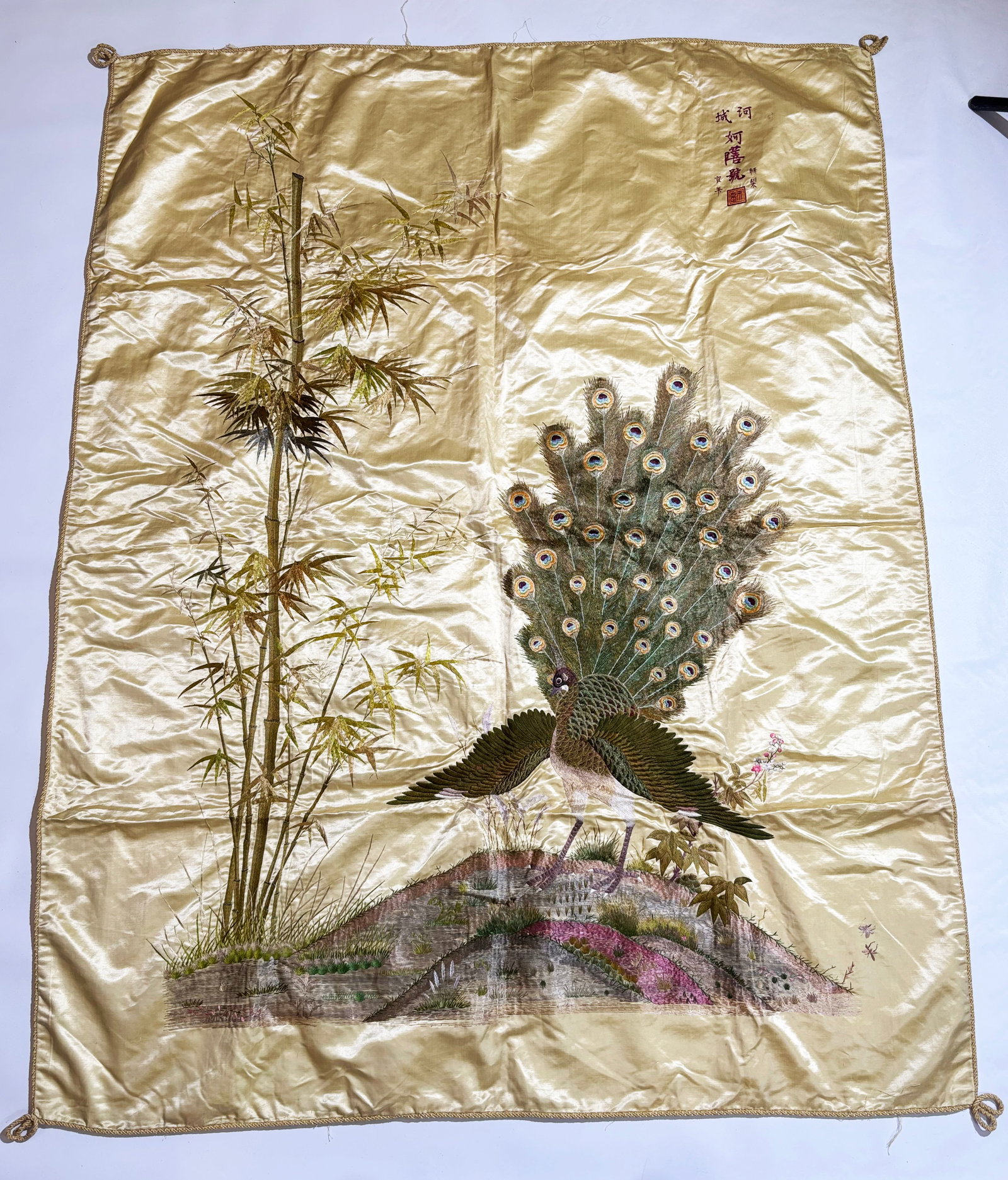 Large Chinese Peacock & Bamboo Silk Embroidery: Chinese or possibly French Vietnam; a Large Peacock & Bamboo Silk Embroidery, the bird displaying his tail feathers standing on a Garden mound with bamboo growing to the side all in colored threads on