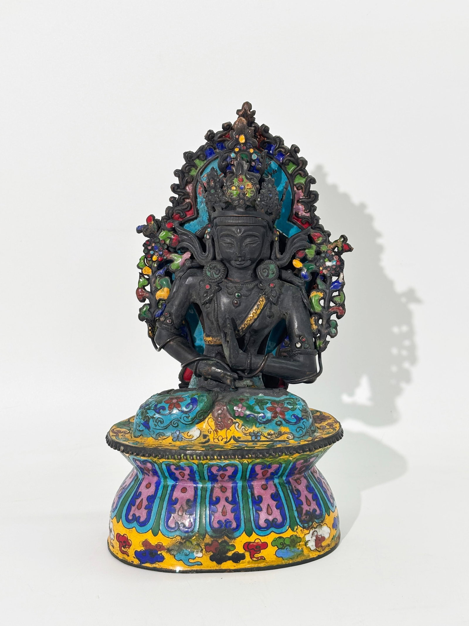 Tibetan Enamel Sheet Copper Seated Avalokiteshvara: Tibetan Enameled Cast and Sheet Copper Seated Avalokiteshvara on sealed double Lotus Throne with a Flower Stem in each hand and a Mandorla to back, the exposed copper in a dark patina. Height 11 3/4 i