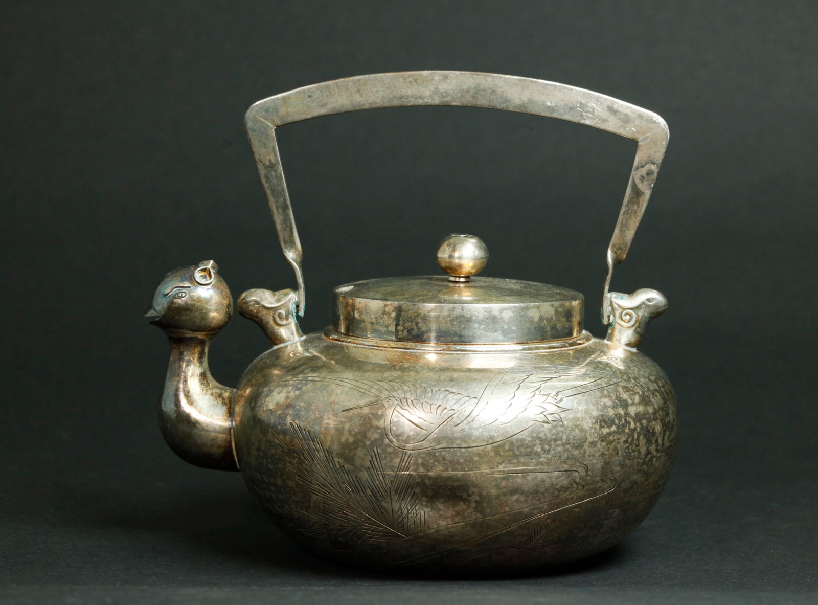 Korean Incised Silver Bird-Head Teapot: Korean Silver teapot incised to 1 side with a Crane & Pine Branch with an archaistic Bird-Head shaped spout and 2 tiny heads holding the overhead handle, with cover and finial; the flat base with a Co