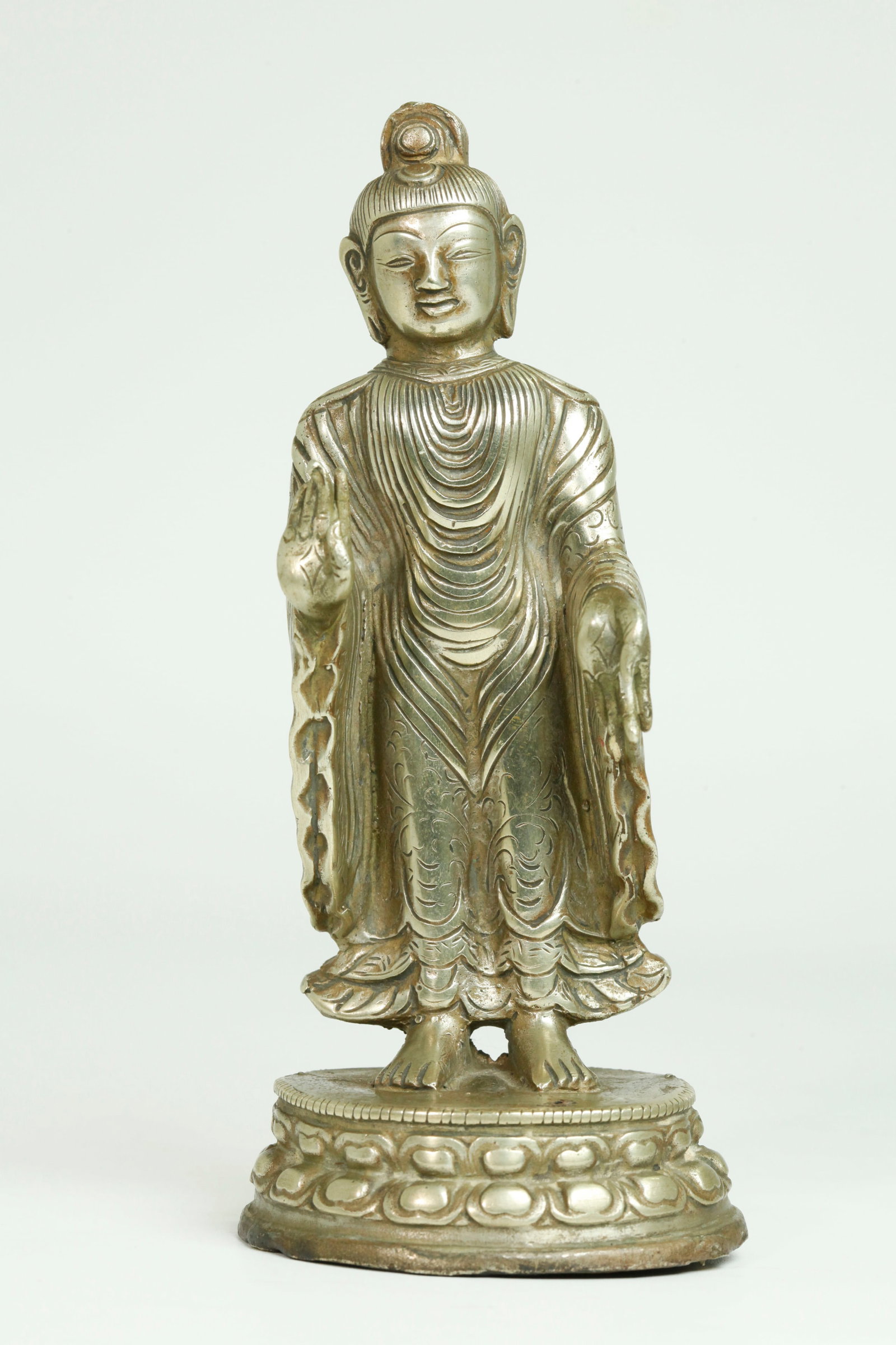 Tibetan White Bronze Standing Buddha Lotus Base: Tibetan White Bronze Standing Buddha on an opened double Lotus Base with draped robe and incised details; scrolling leaves to back of robe over a small inscription to back of base in Tibetan. Height 6