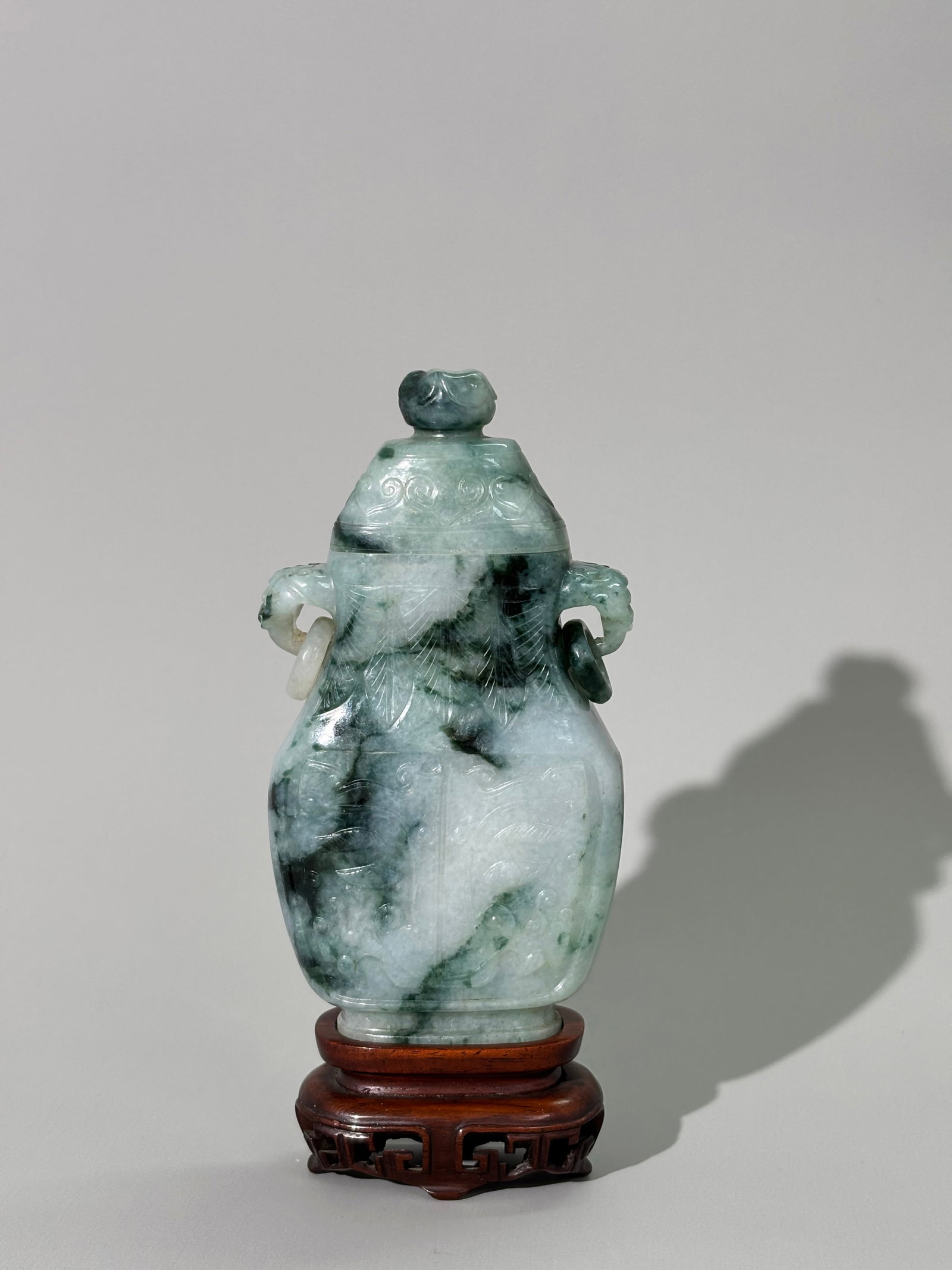 Fine Chinese Qing White Green Jadeite Covered Urn: Fine Chinese Qing Dynastry translucent White to Dark Green Jadeite Covered Urn with animal head loop and integral loose ring handles, the sides well carved with Taotie Masks; with hard wood stand on 4